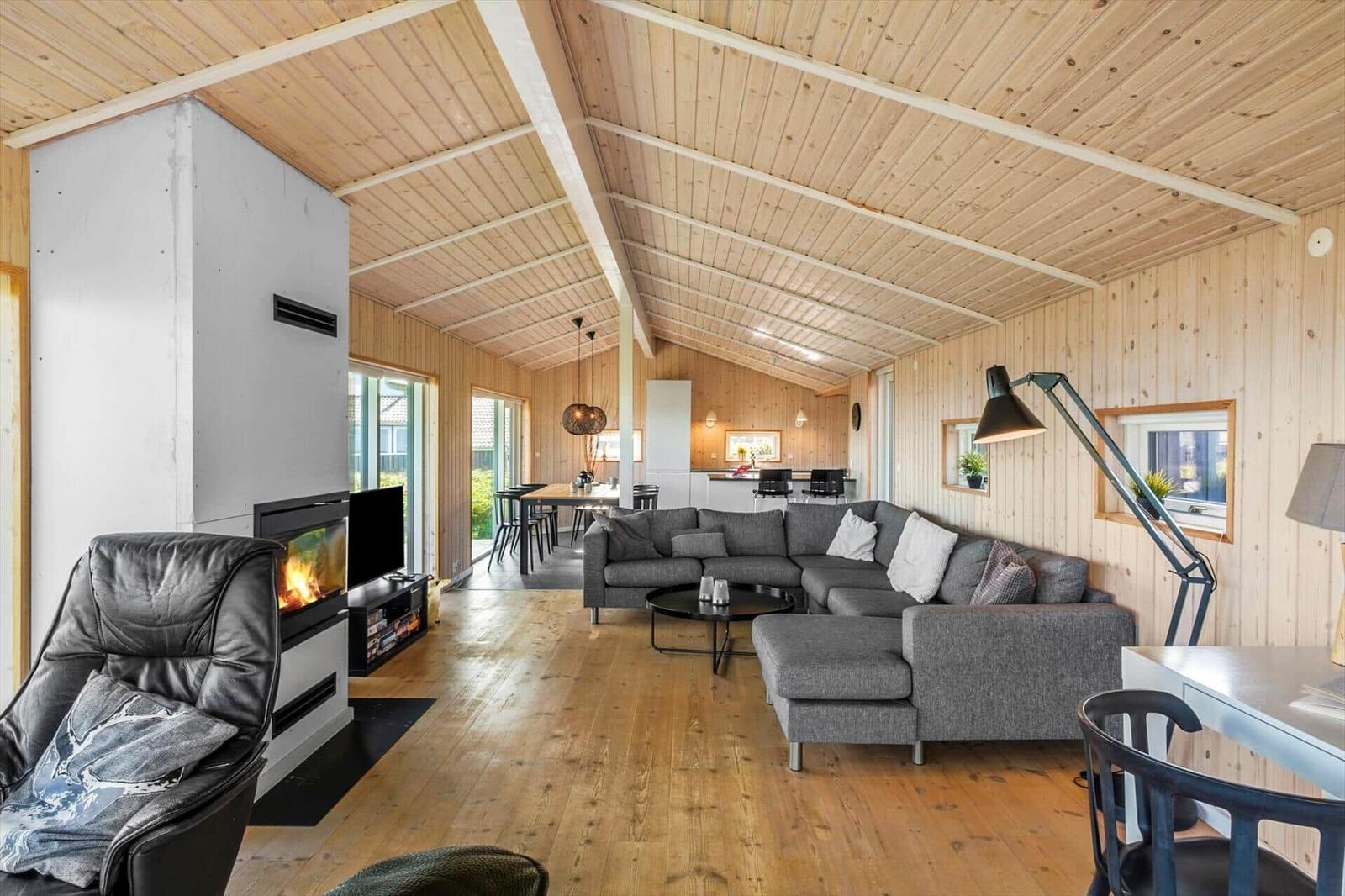 Wohnzimmer mit Kamin, Sofa und Essbereich unter Holzdecke.