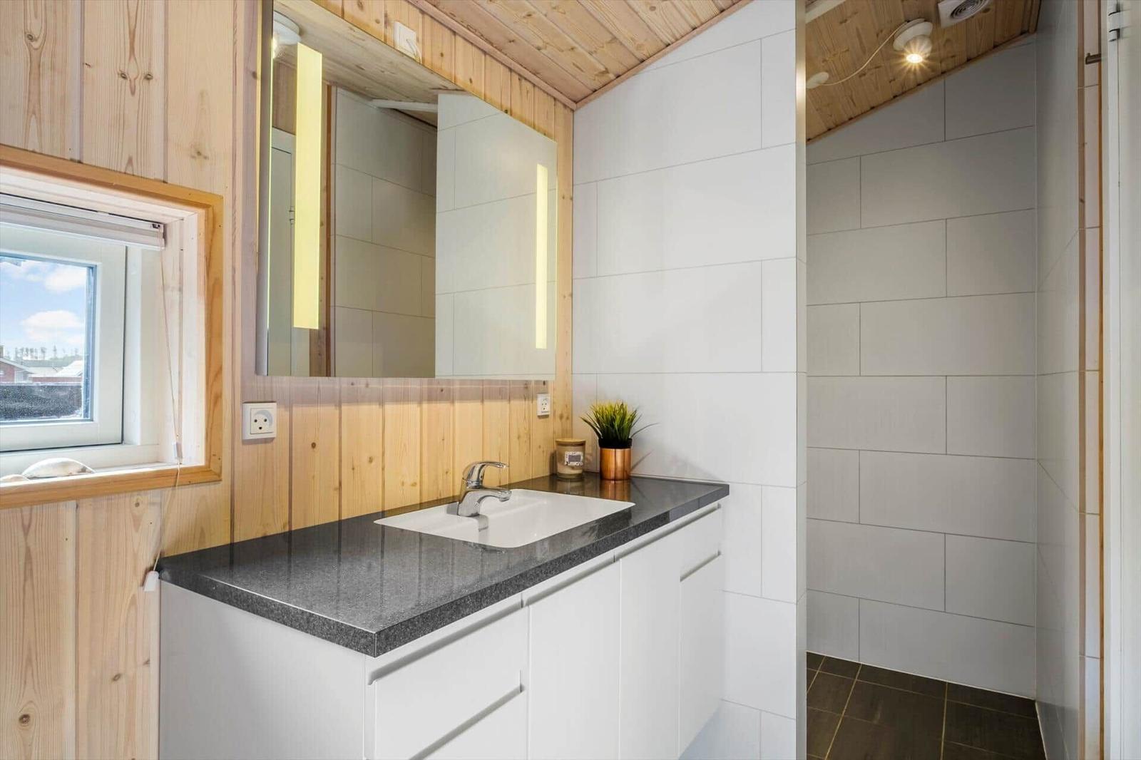 Badezimmer mit Waschtisch, Spiegel und Dusche. Holzwände und weiße Fliesen.