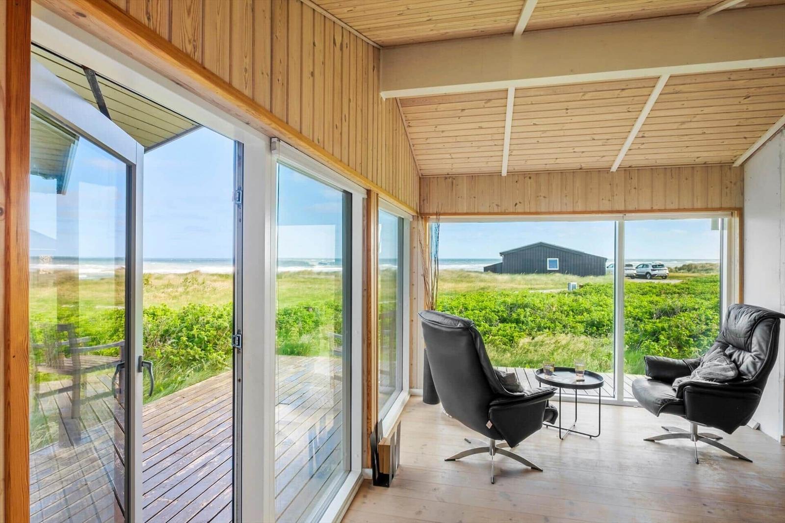 Terrasse mit zwei schwarzen Sesseln und Blick auf Grasland und Strand.