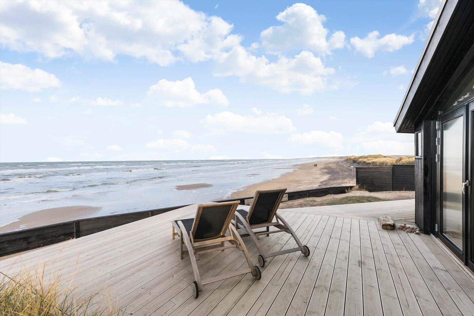 Terrasse mit zwei Liegestühlen direkt am Strand und Blick aufs Meer.