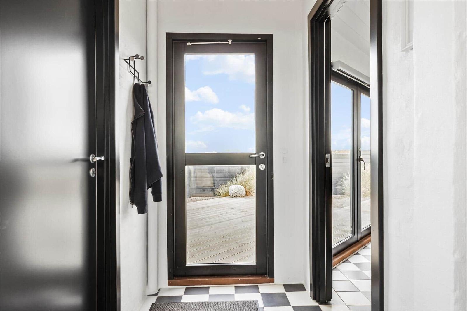 Eingang mit schwarzem Tür- und Fensterrahmen, schwarz-weißem Boden und Blick auf Balkon mit Holzdecke.