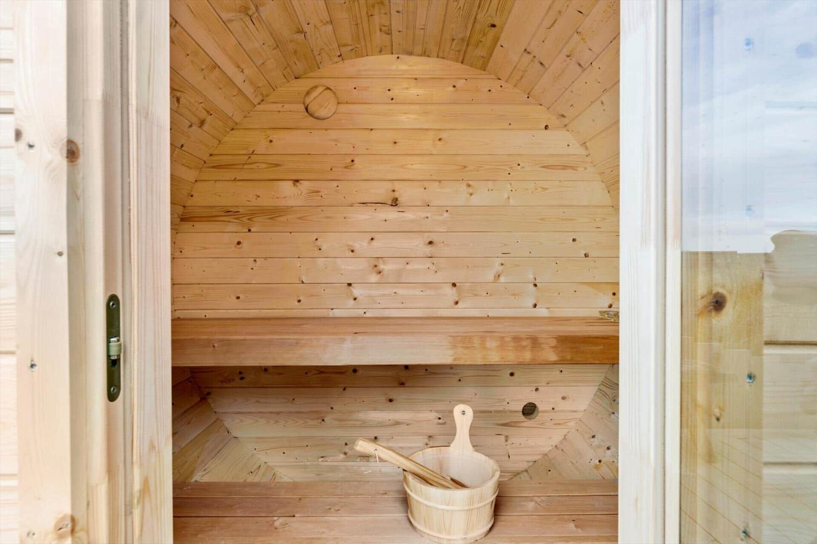 Holzsauna mit Sitzbank und Eimer mit Besen.