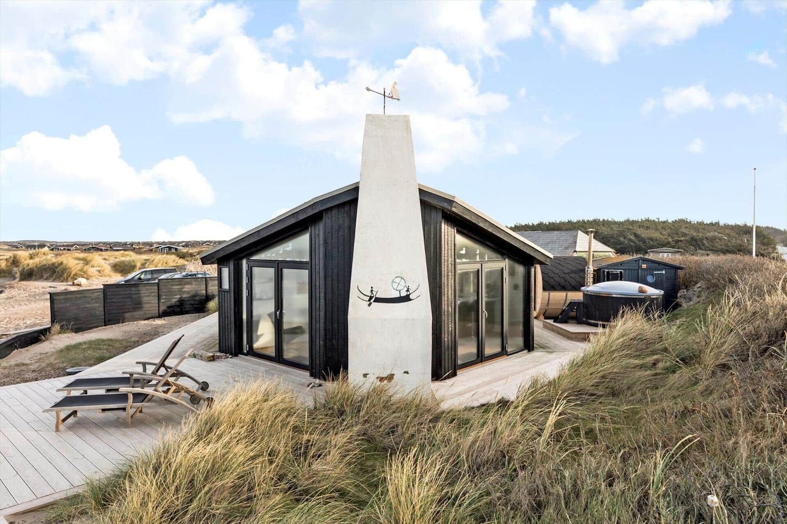 Moderne Strandhütte mit Terrasse, Liegestühlen und Dachterrasse. Hintergrund: Dünen und Wald.