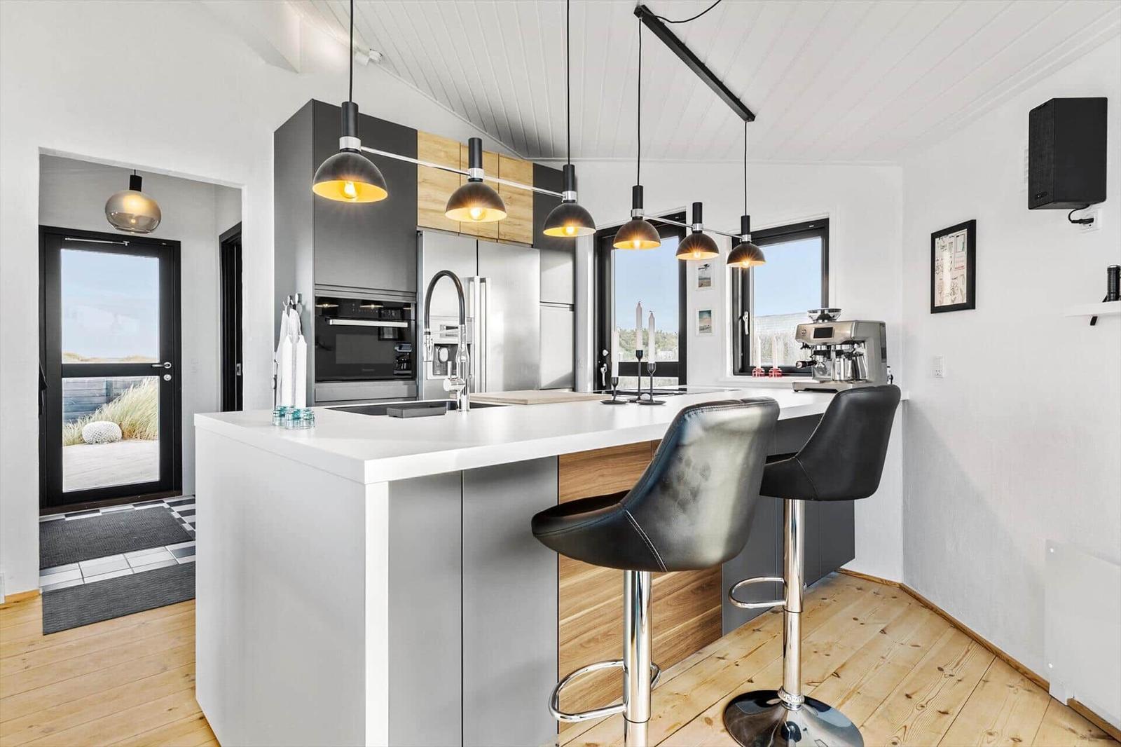 Moderne Küche mit Kücheninsel, schwarzen Barhockern und integriertem Kühlschrank.