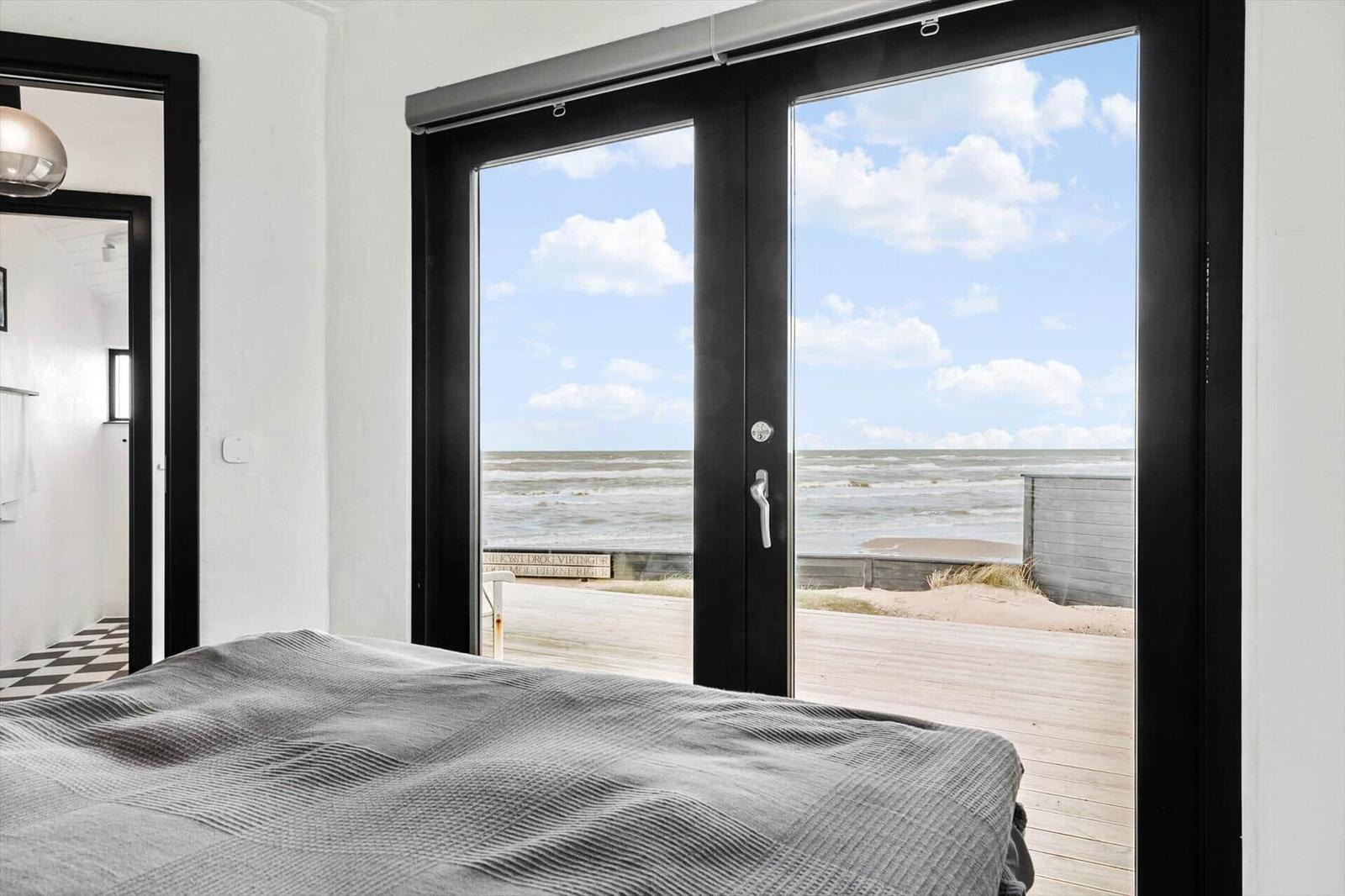 Schlafzimmer mit Blick auf Strand und Meer durch große Glastüren.