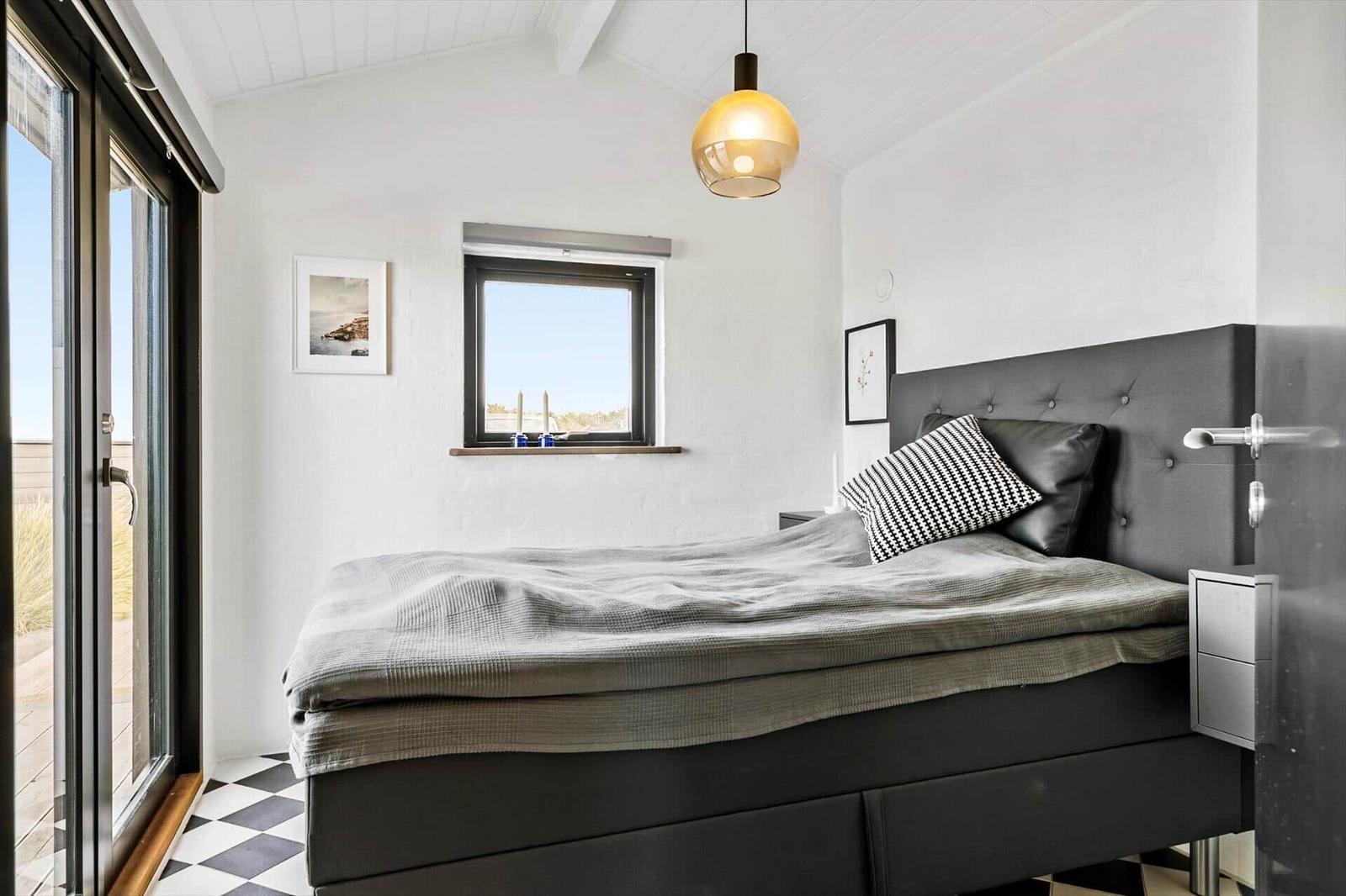 Schlafzimmer mit Bett, Fenster und Glastür. Schwarze Möbel und weißer Boden.