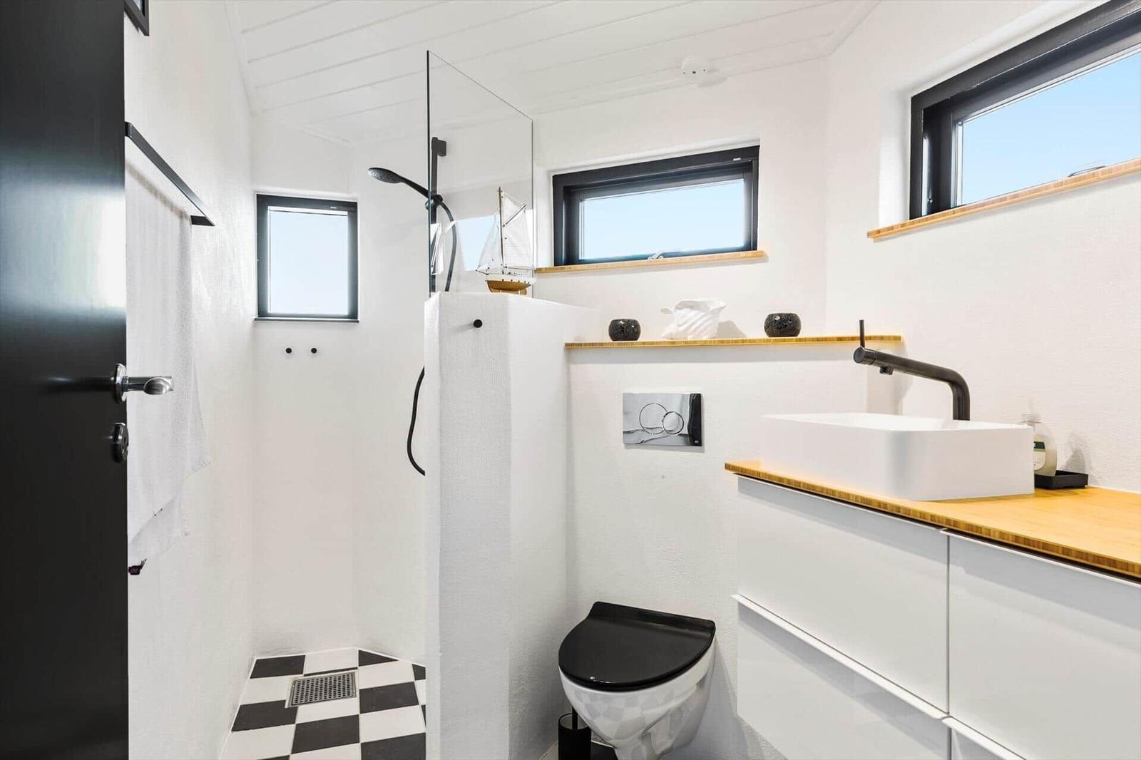 Badezimmer mit Dusche, Waschbecken und Toilette. Schwarze Fenster und schwarz-weiße Fliesen.