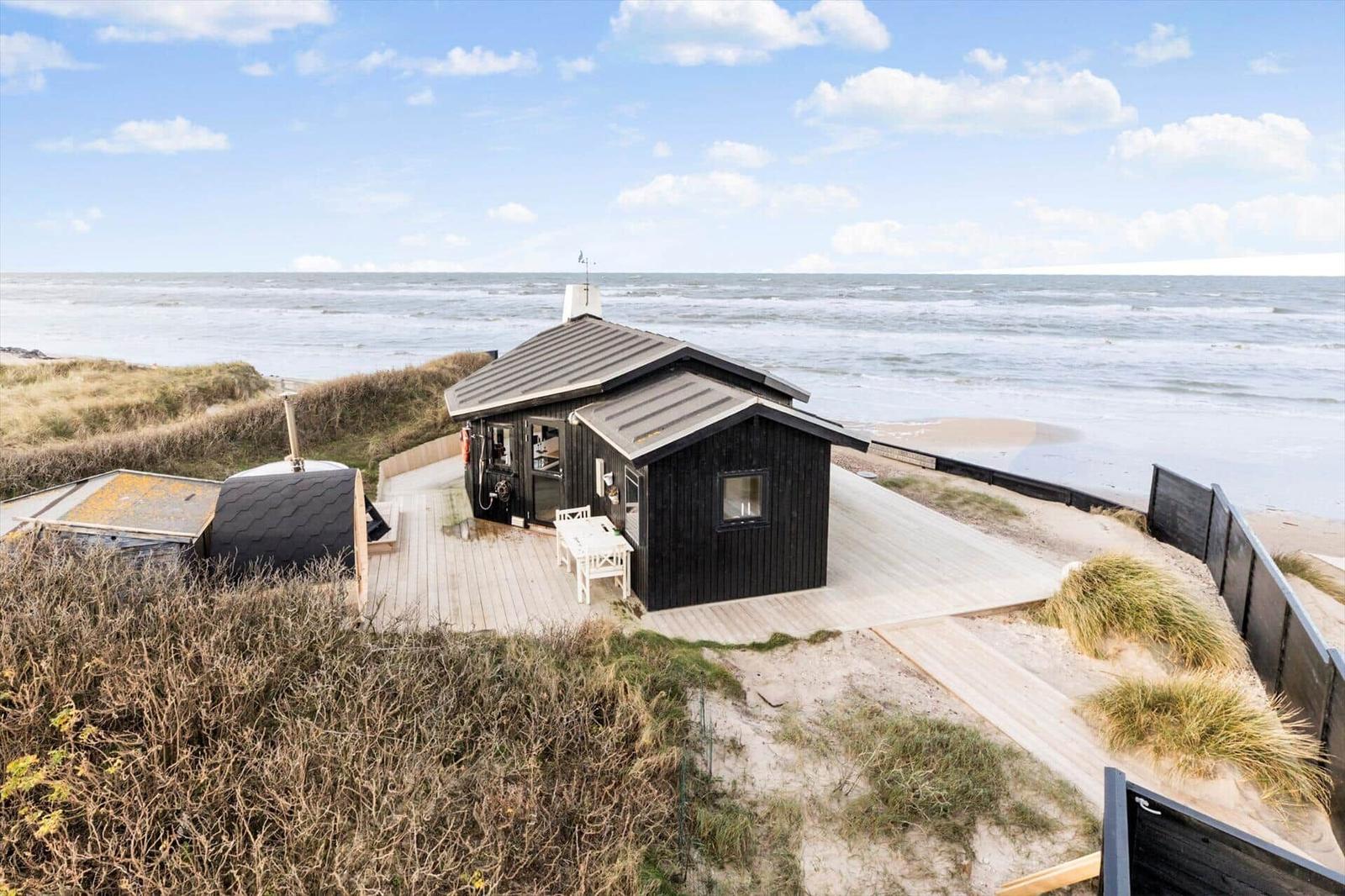Schwarze Strandhütte mit Terrasse direkt am Meer.