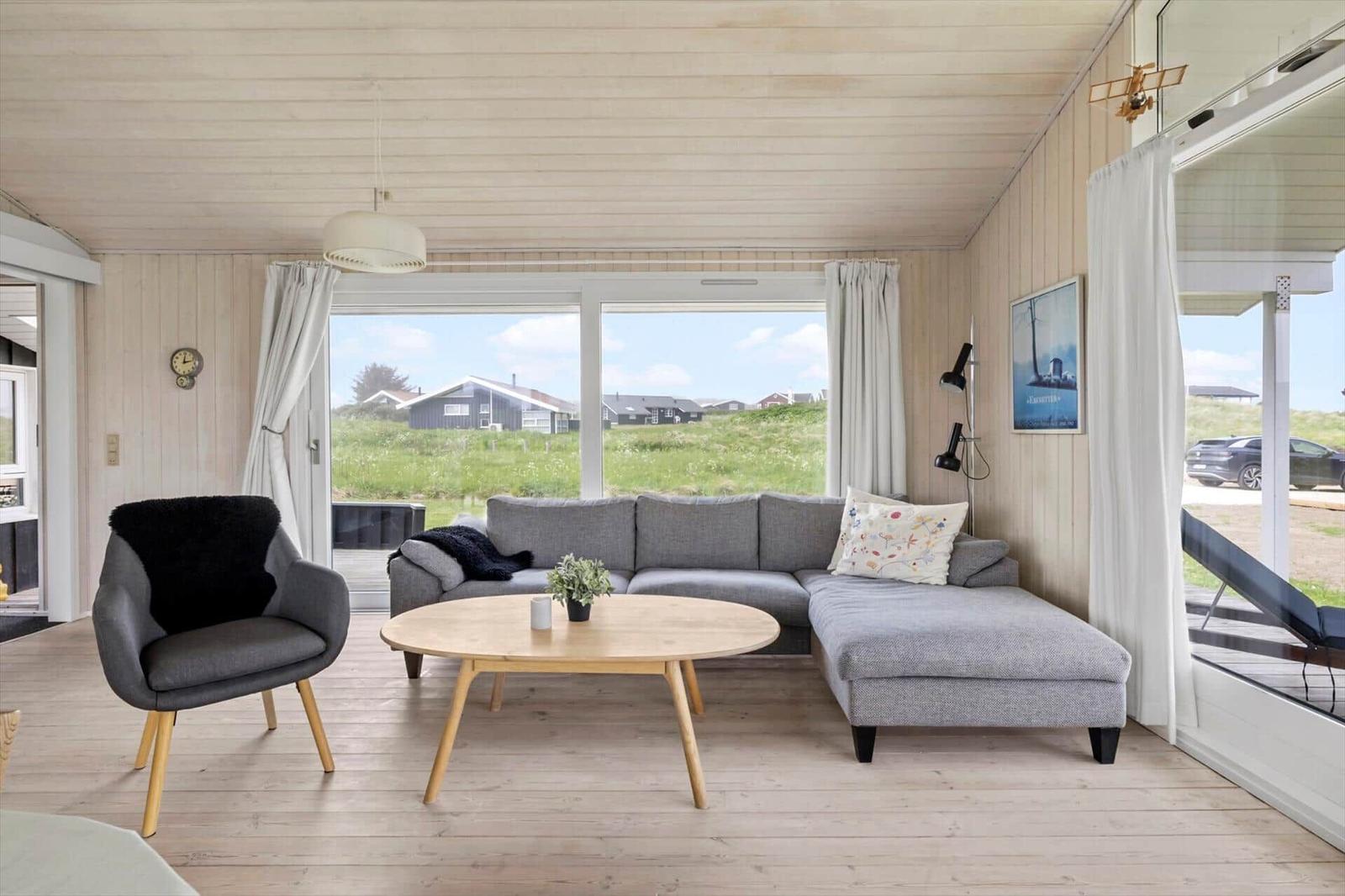 Wohnzimmer mit grauem Sofa, runden Tisch und Blick auf Grünland.