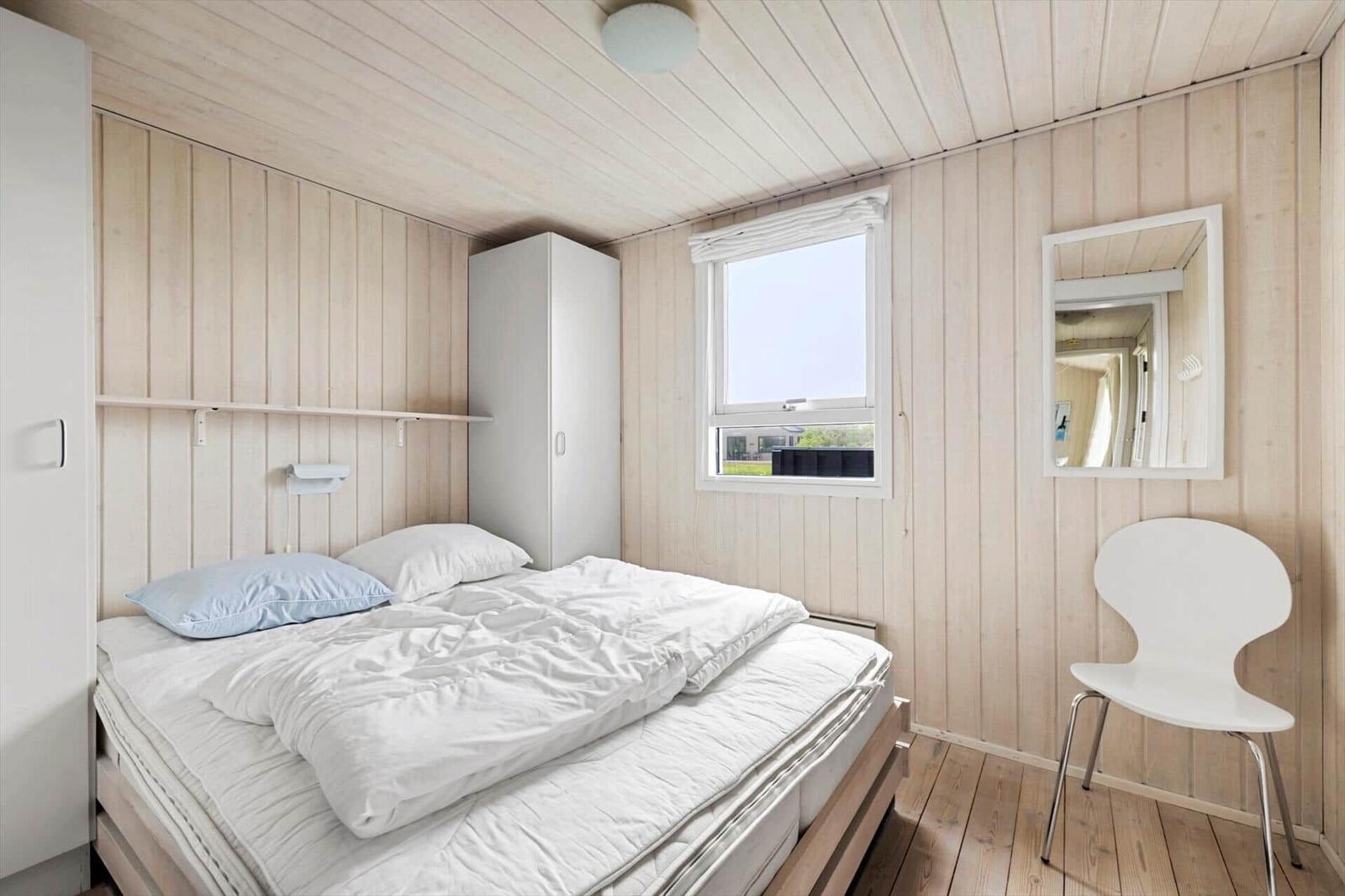 Schlafzimmer mit Bett, Kleiderschrank, Spiegel und Stuhl an Holzwand.