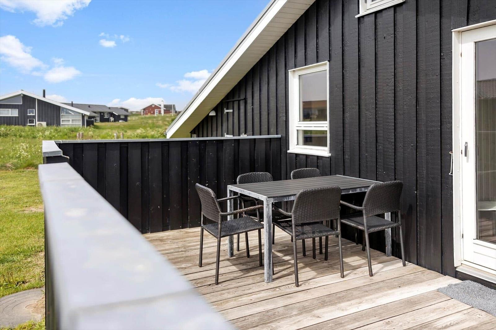Terrasse mit Tisch und Stühlen an schwarzem Holzhaus mit Blick auf Grasland.