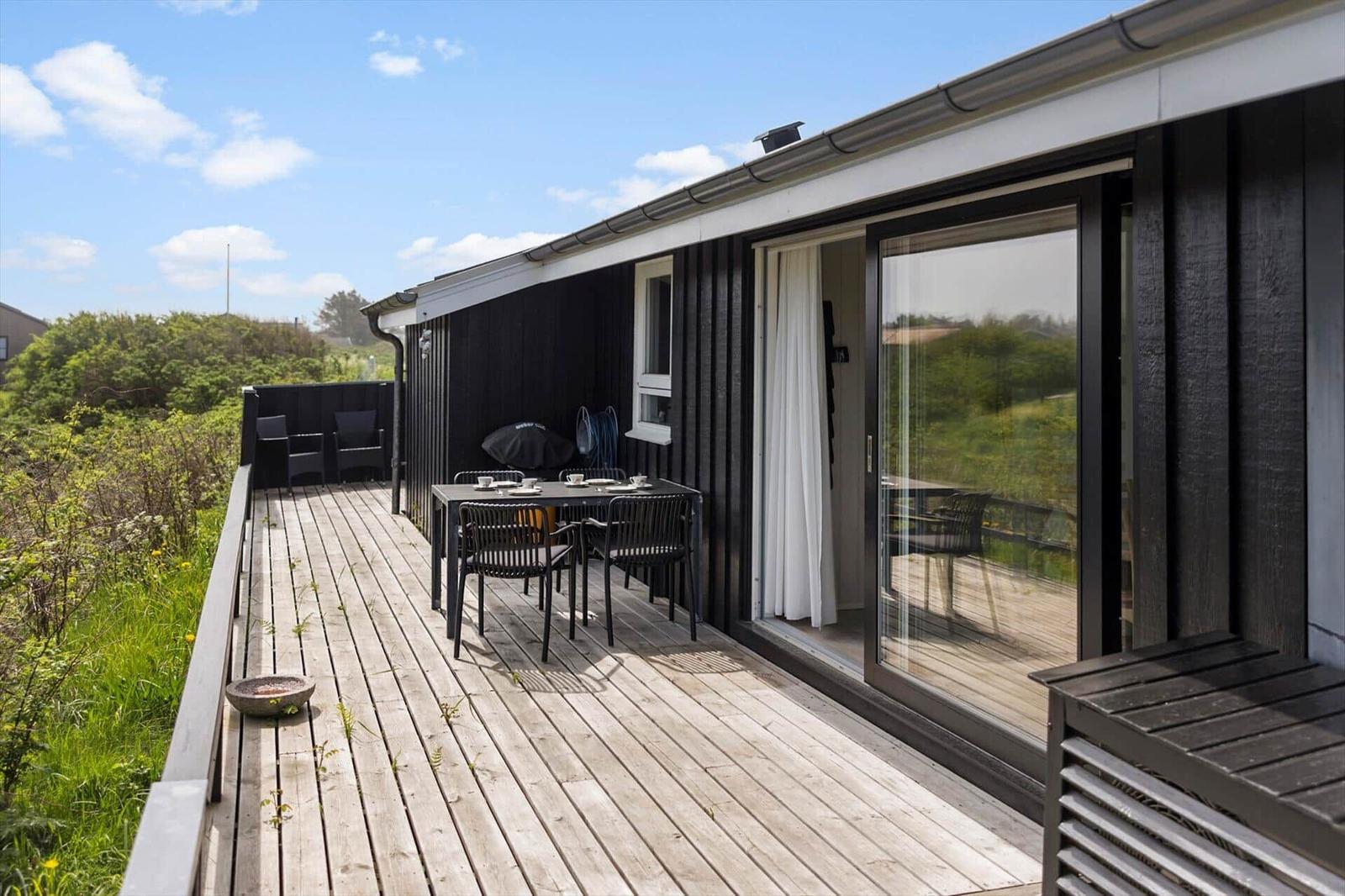 Terrasse mit Tisch, Stühlen und Grill. Blick auf grüne Landschaft. Glasfront zur Wohnung.