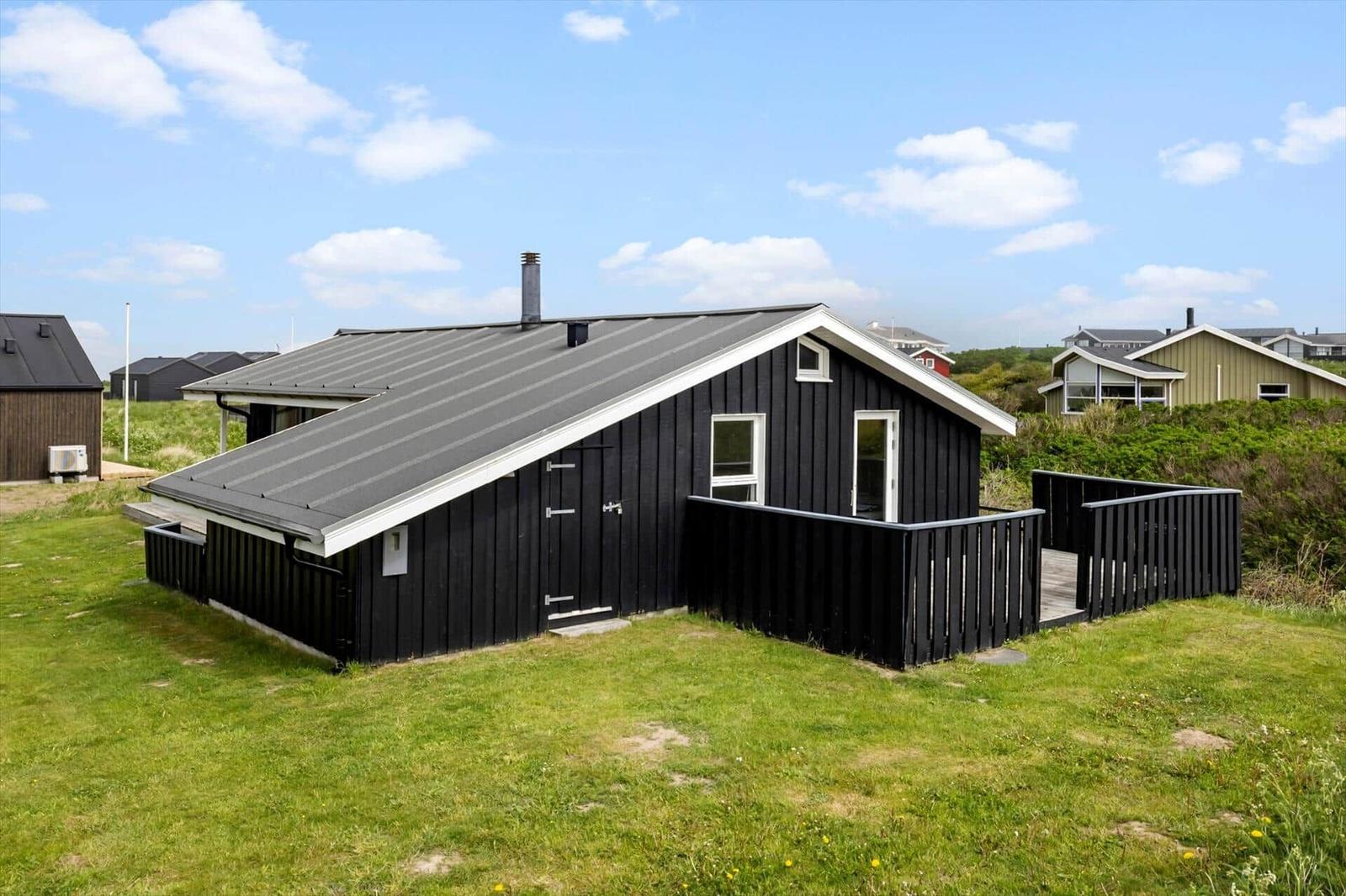 Schwarze Holzhütte mit Balkon und Dachgaube auf grünem Grund.