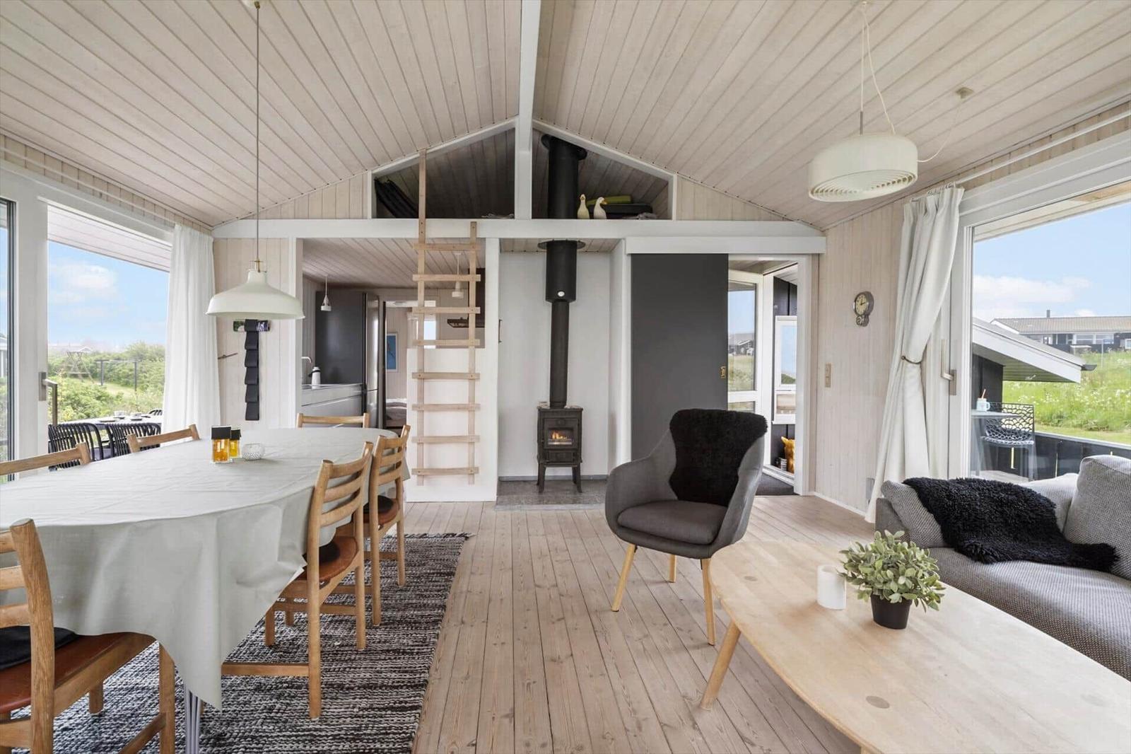 Wohn- und Essbereich mit Holzboden, Esstisch, Sofa und Kaminofen. Helle Fensterfronten mit Blick.