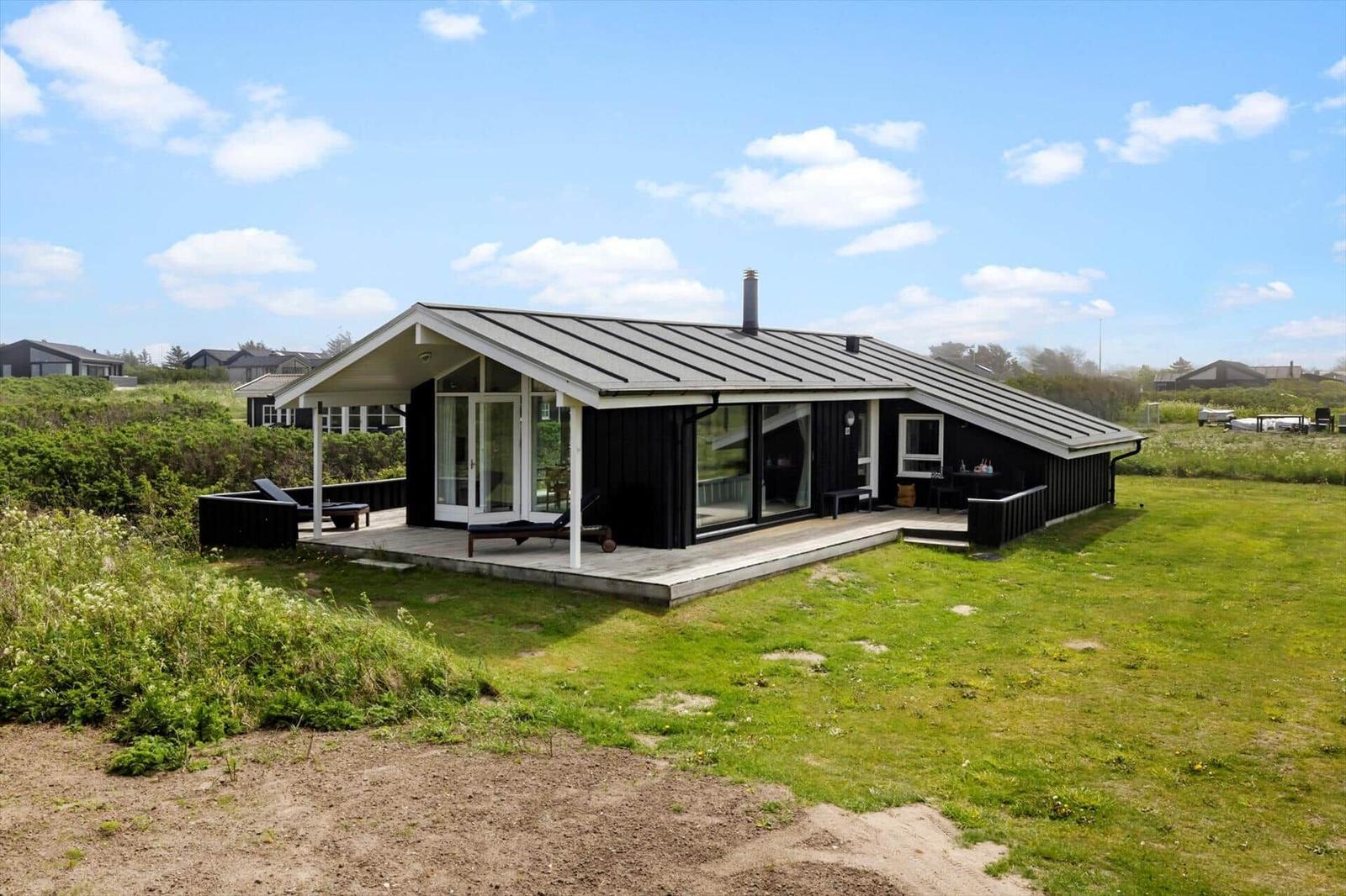Moderne Holzhütte mit Terrasse und Garten. Blick auf das Haus unter blauem Himmel.