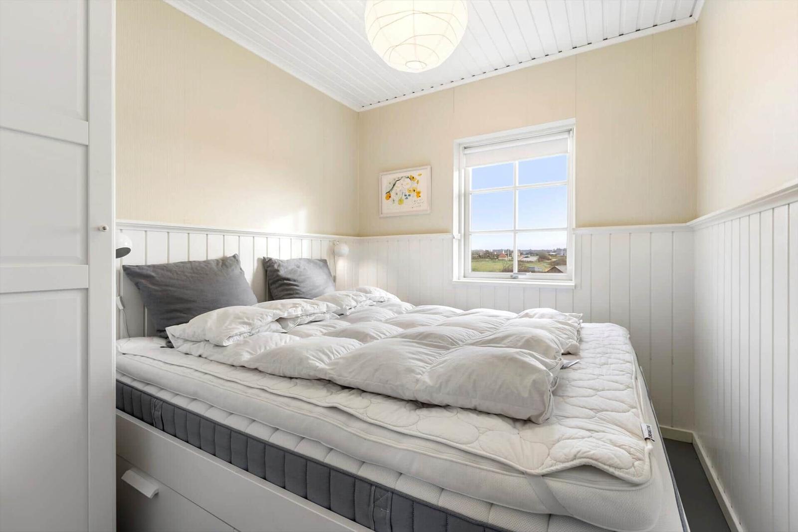 Schlafzimmer mit Bett, Fenster und Decke. Wandverkleidung und Lampen sichtbar.
