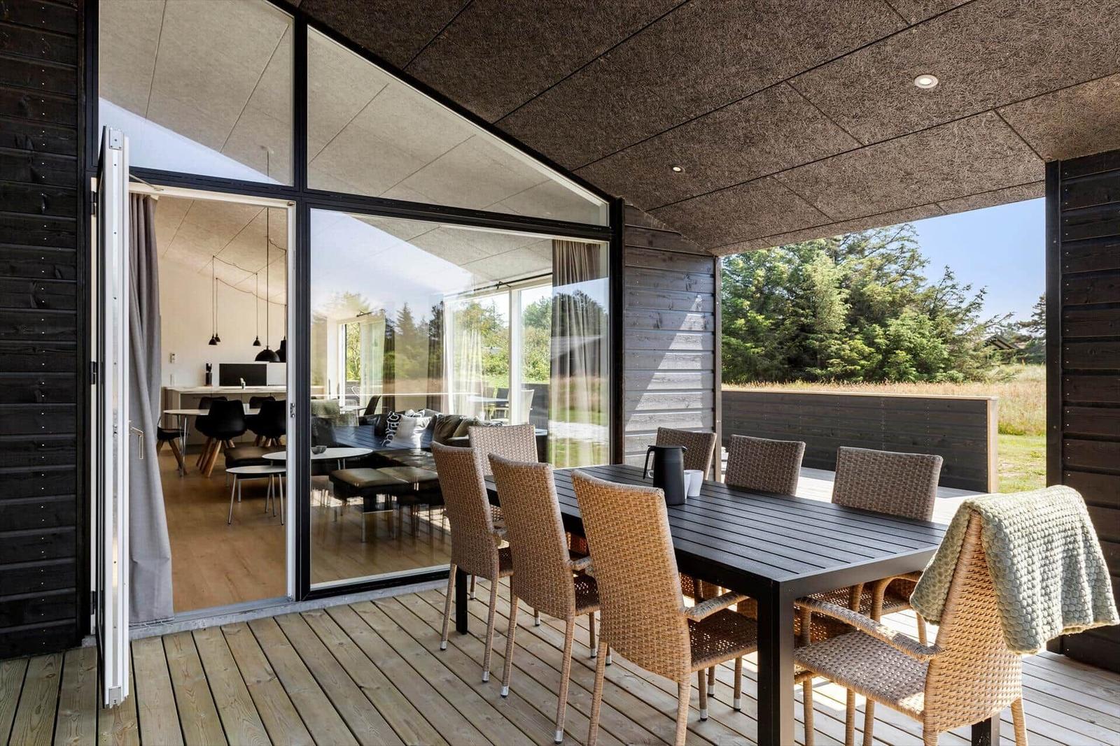 Terrasse mit Esstisch und Stühlen, Blick ins Innere und auf Grünfläche.