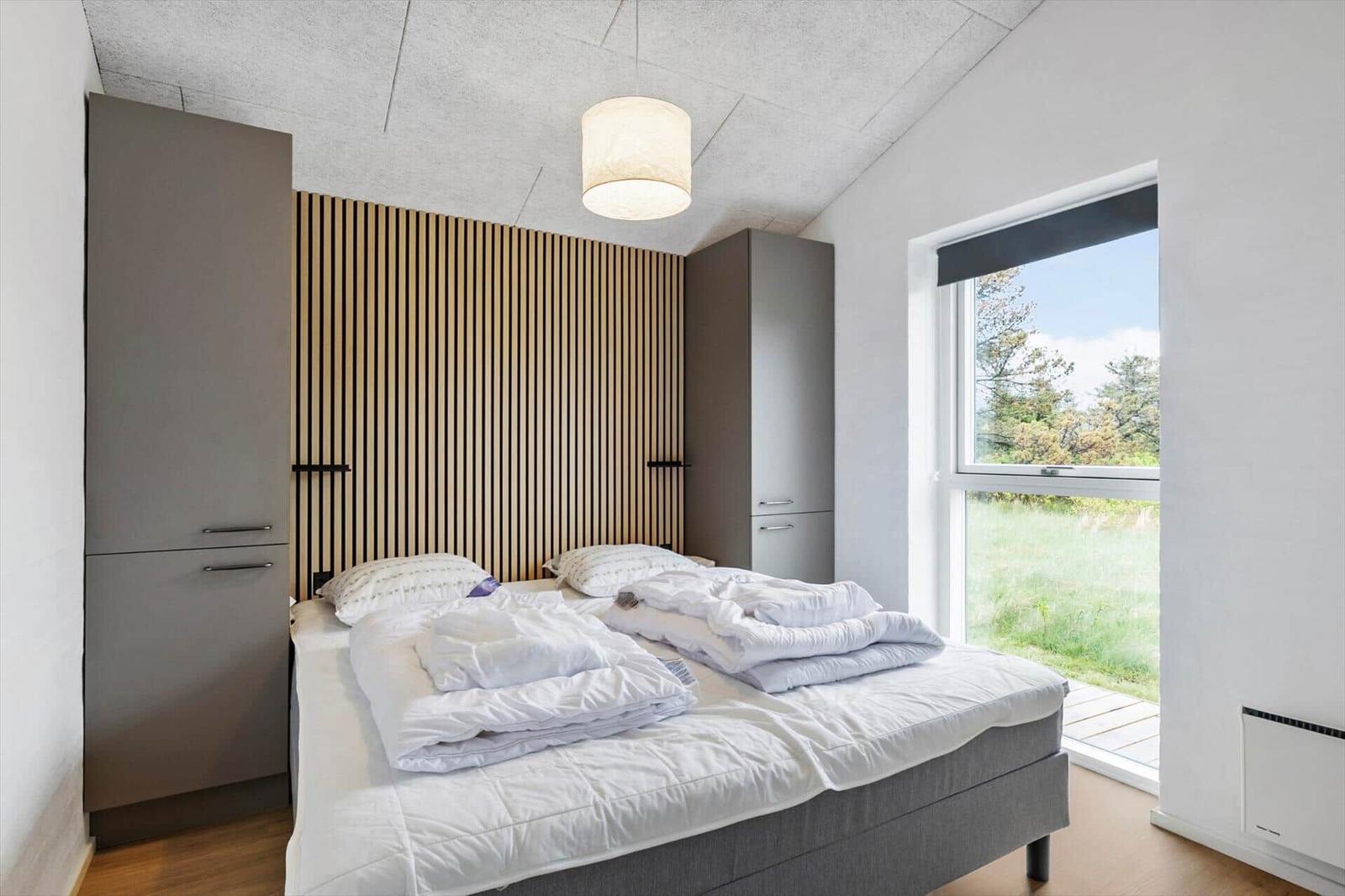 Schlafzimmer mit Bett, Kleiderschränken und Fenster zum Garten.