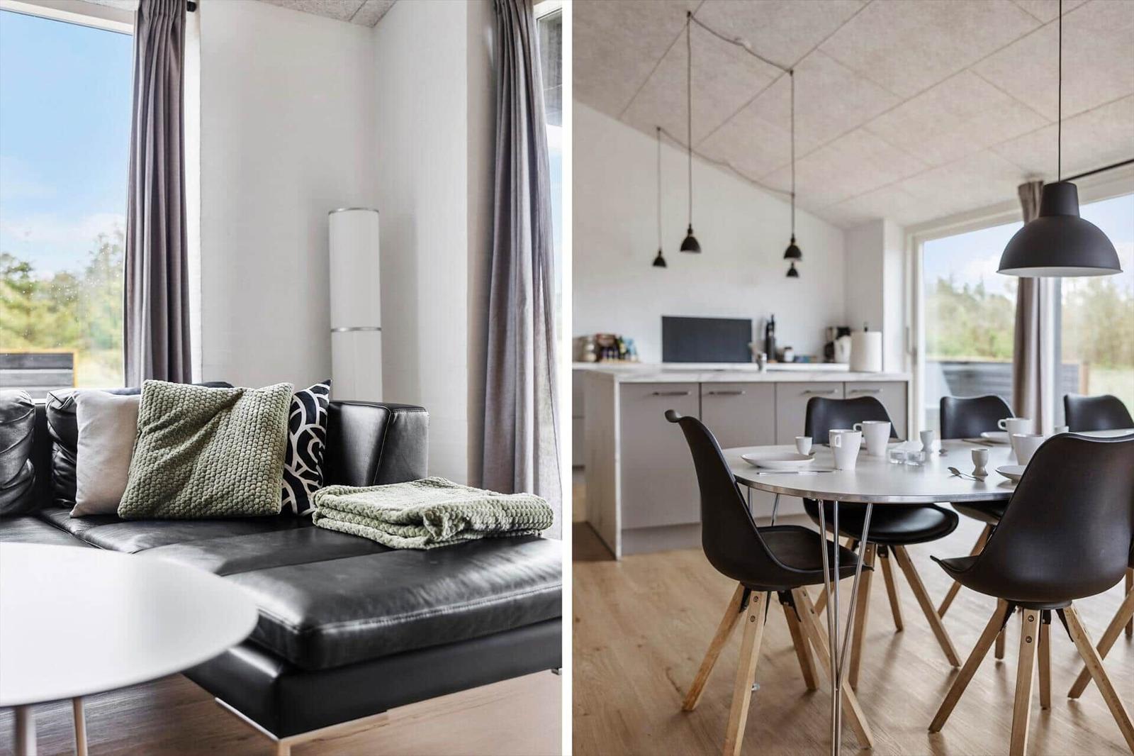 Schwarzes Sofa mit Kissen und Decke. Essbereich mit Tisch, Stühlen und Küchenzeile.