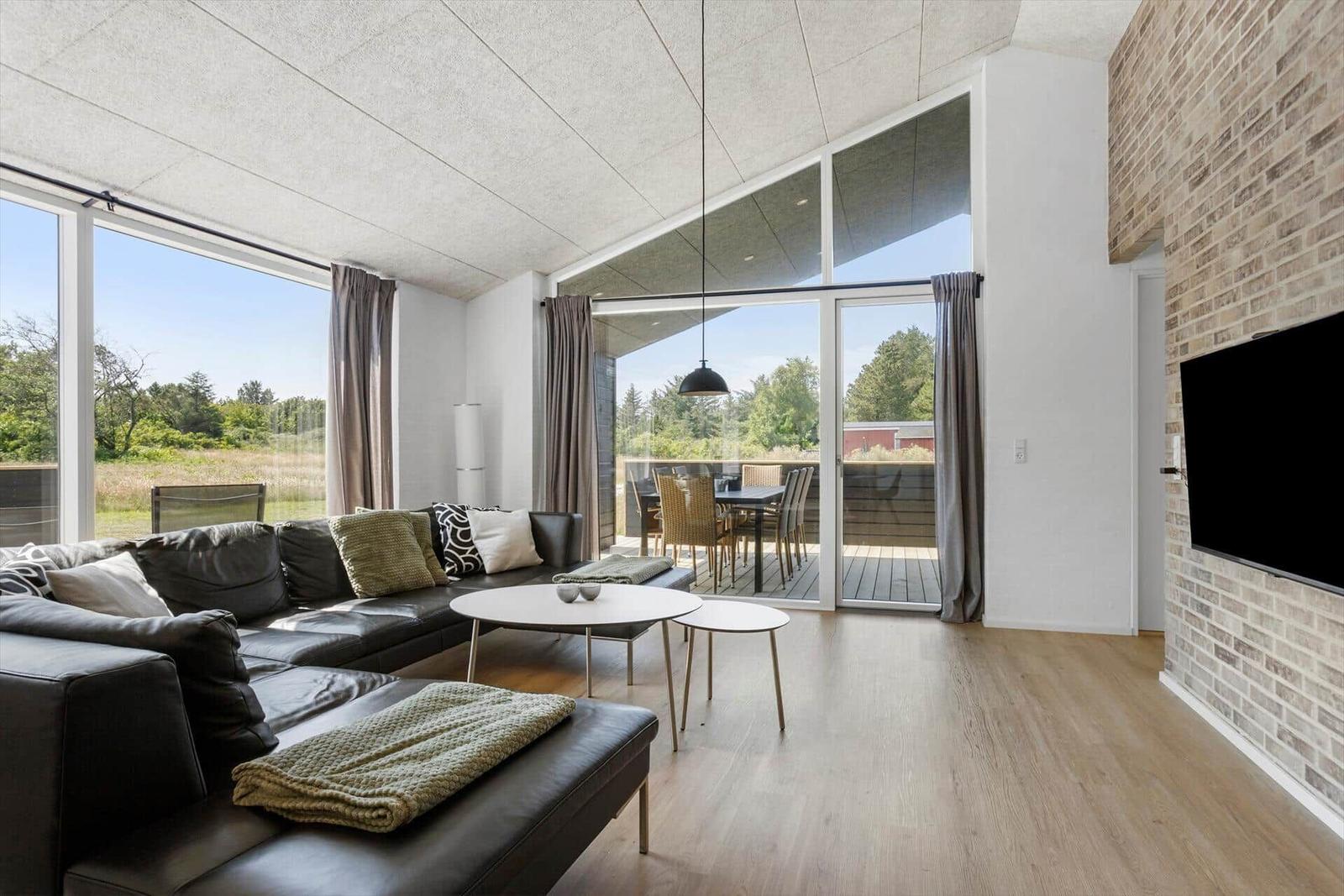 Wohnzimmer mit Ledersofa, Glasfront und Holzboden. Fernseher an Ziegelwand.