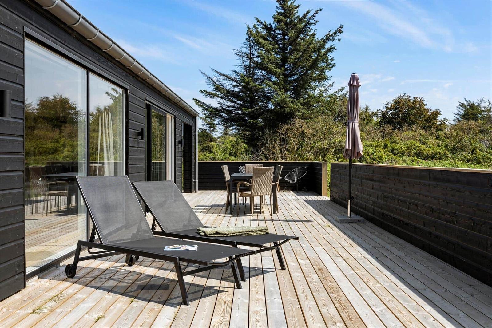 Terrasse mit Liegen, Tisch und Stühlen. Hintergrund: Baum und Himmel.