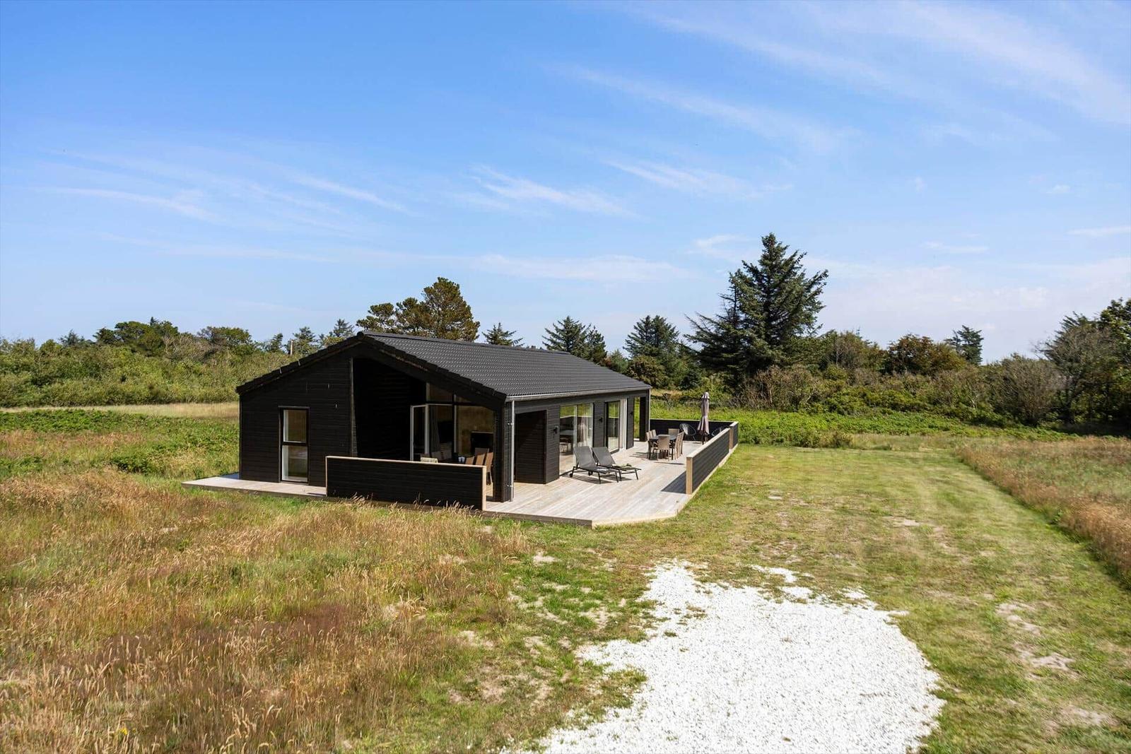 Moderne Holzhütte mit Terrasse, Garten und Blick auf Wald.