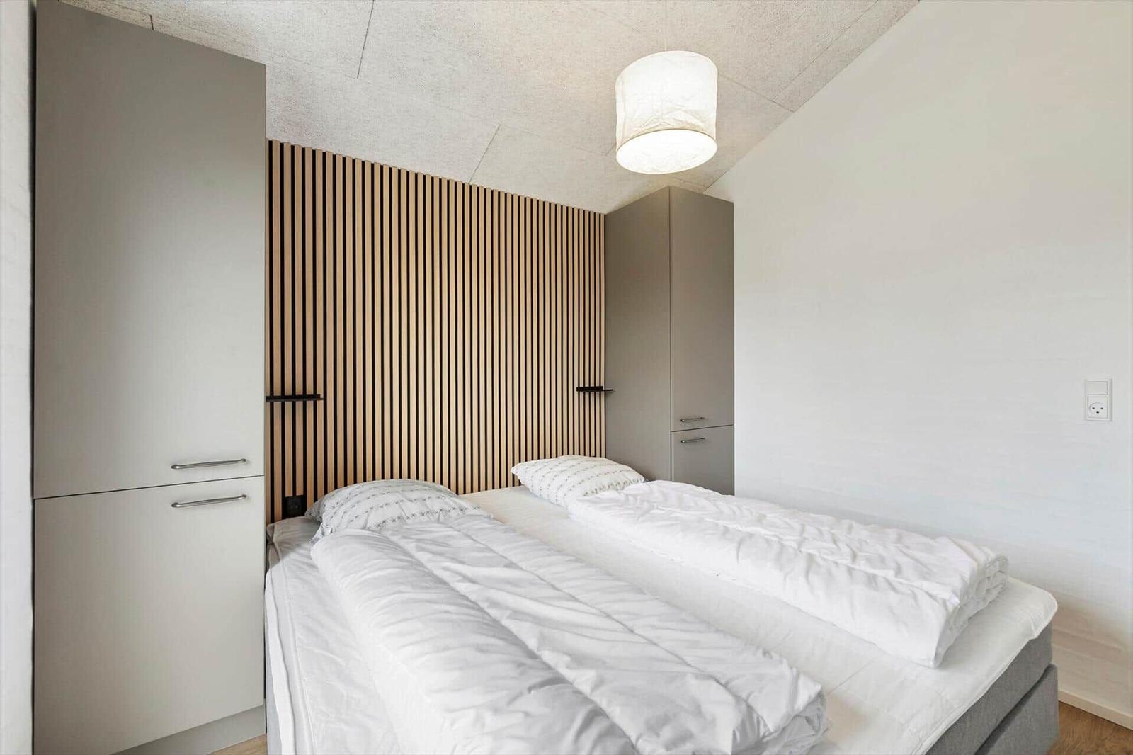 Schlafzimmer mit Doppelbett, Holzpaneelen und integrierten Schränken.
