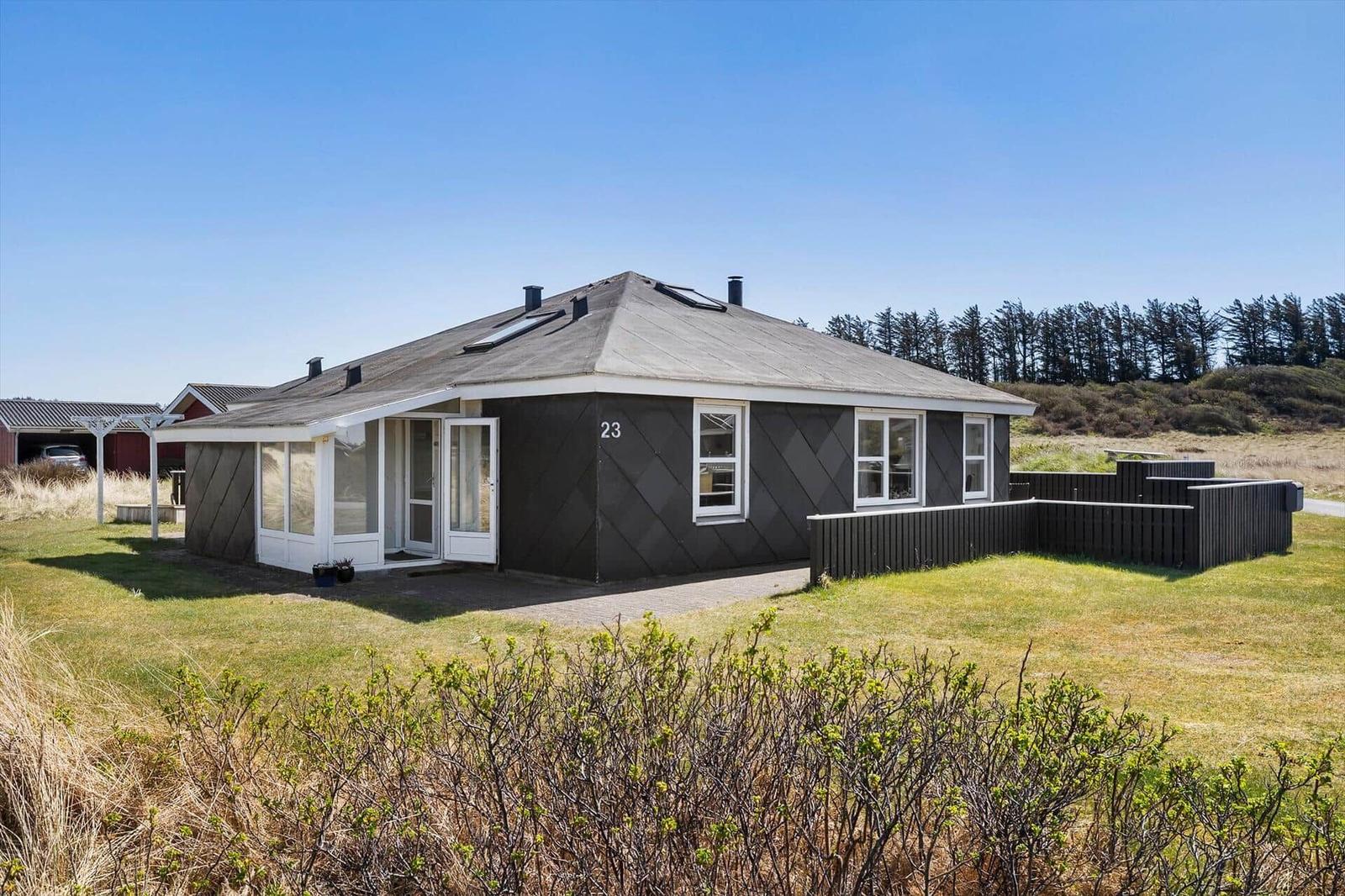 Ein dunkelgrauer Ferienhaus mit weißem Rahmen und Garten. Nummer 23.