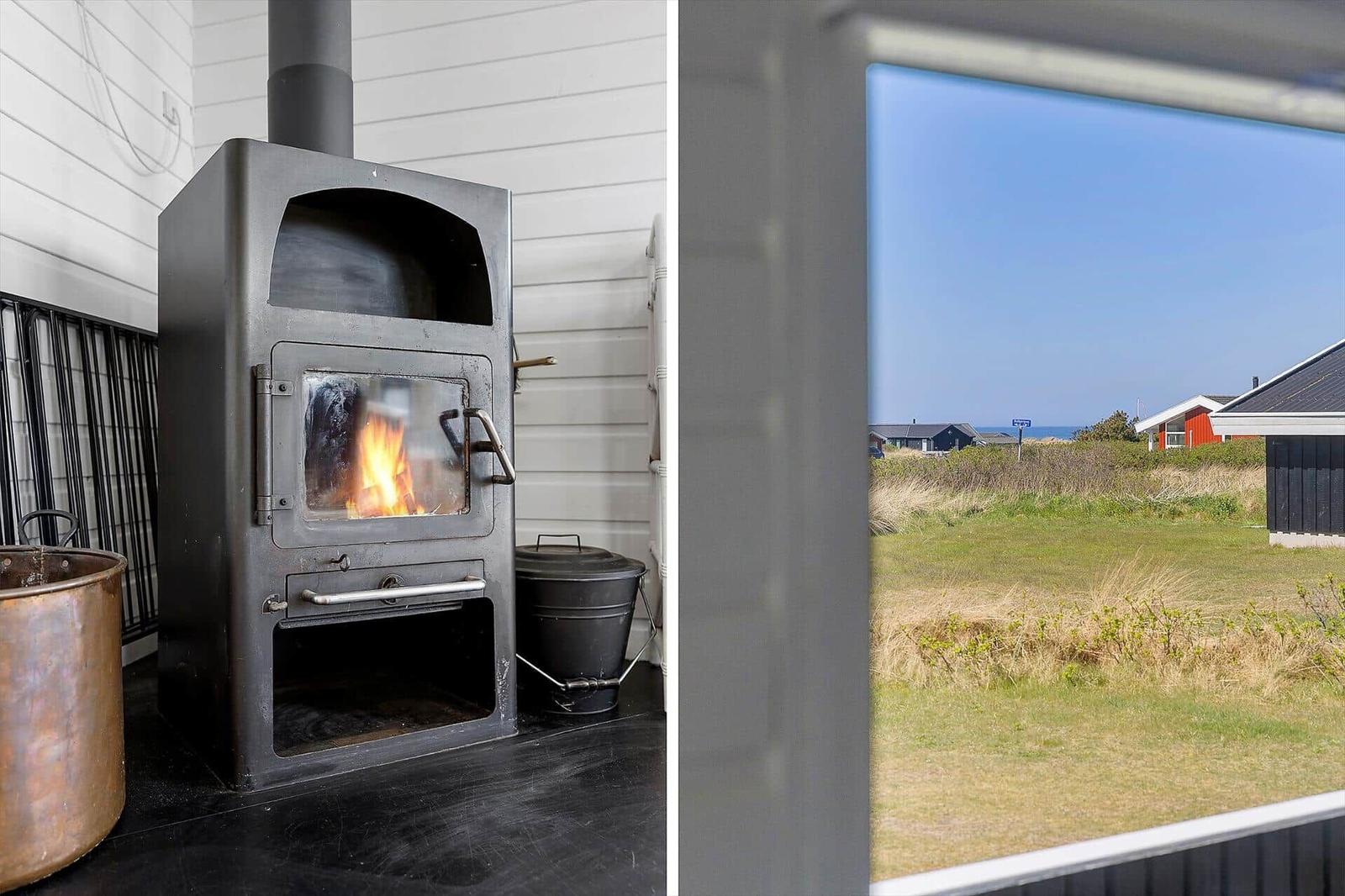 Kaminofen mit brennendem Feuer und Blick auf Grasland mit Häusern im Hintergrund.