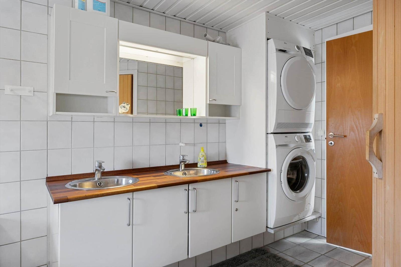 Waschraum mit Waschmaschine und Trockner, zwei Waschbecken und Spiegelschrank.