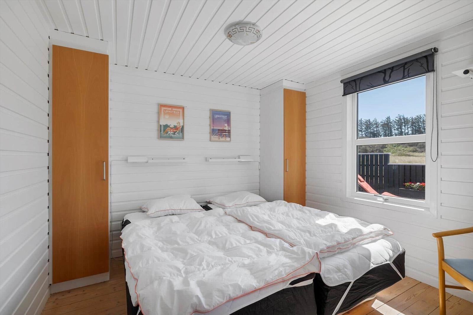 Schlafzimmer mit Doppelbett, Fenster und Holzmöbeln.