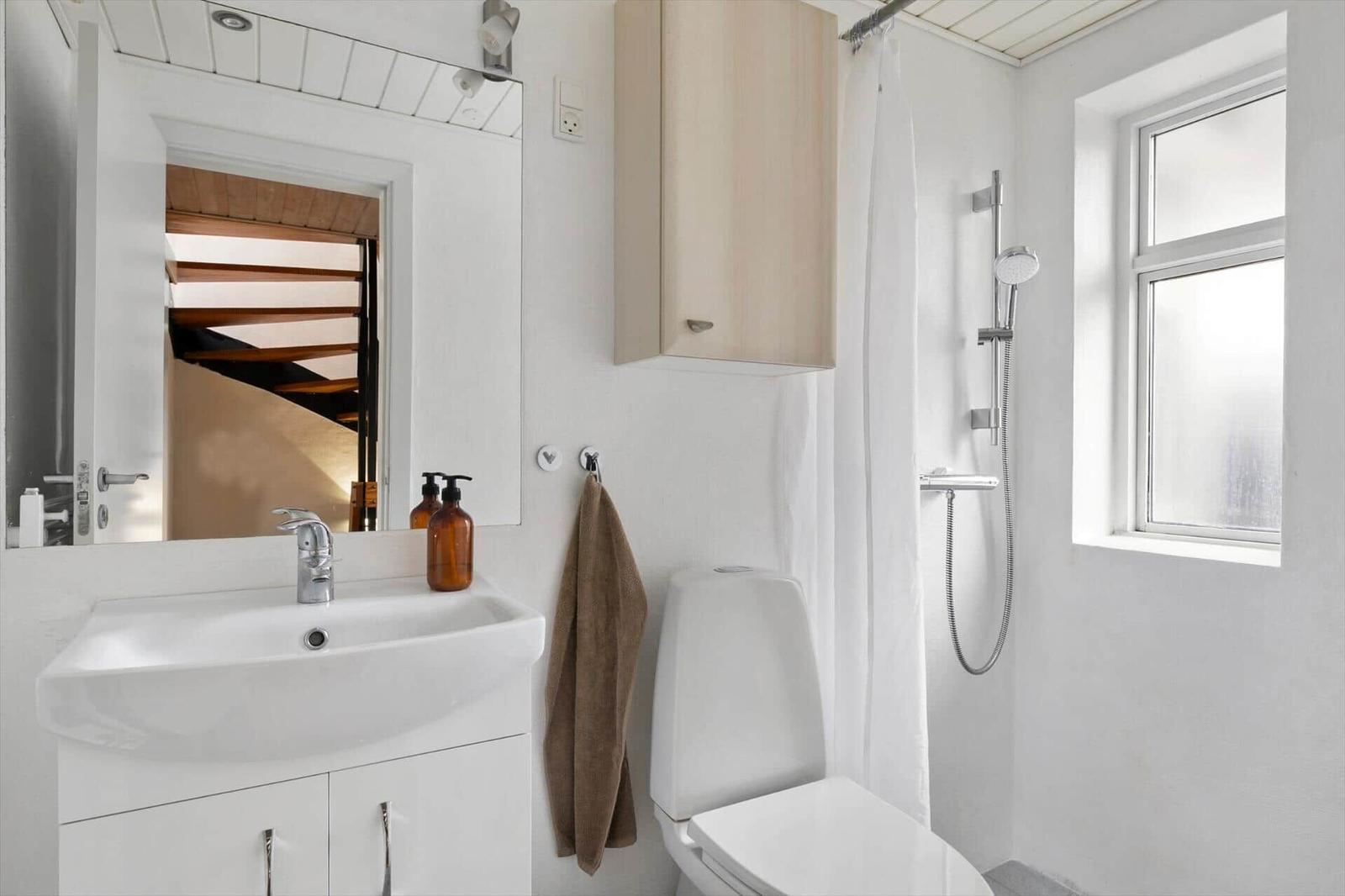 Badezimmer mit Waschbecken, Toilette und Dusche. Spiegel und Fenster sichtbar.