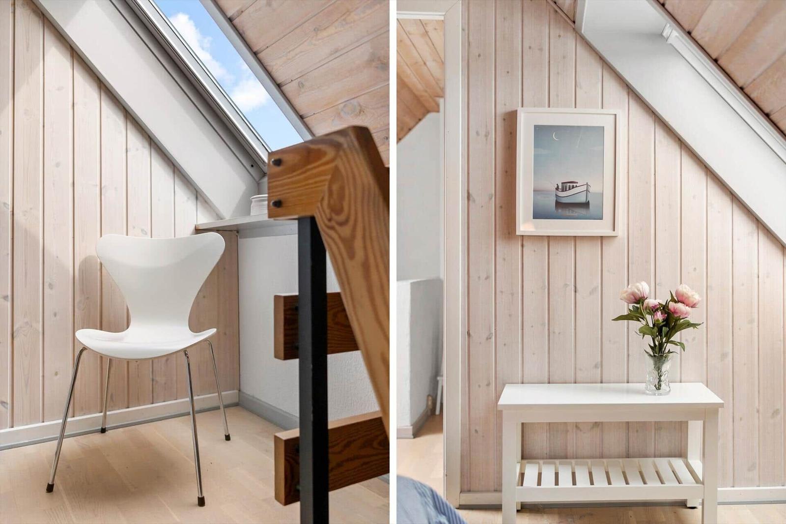 Dachgeschosszimmer mit Holzwand, Fenster und Stuhl. Nebenraum mit Tisch, Blumen und Bild.
