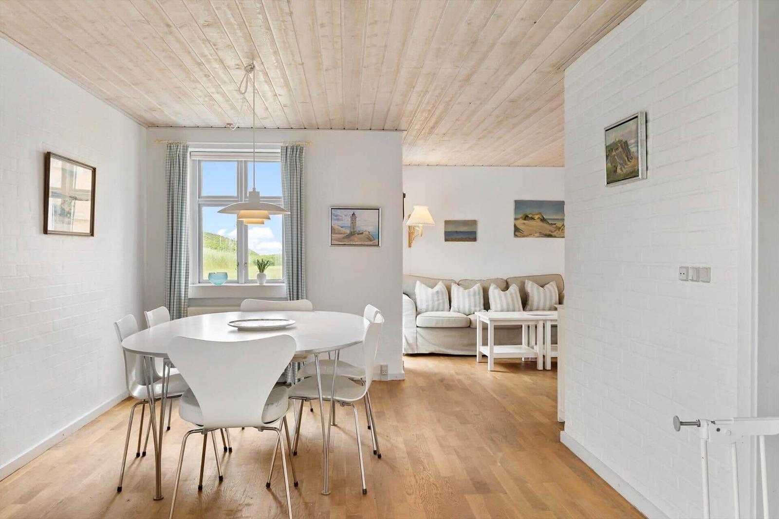 Esszimmer mit weißem Tisch und Stühlen. Wohnzimmer mit Sofa und Couchtisch im Hintergrund.