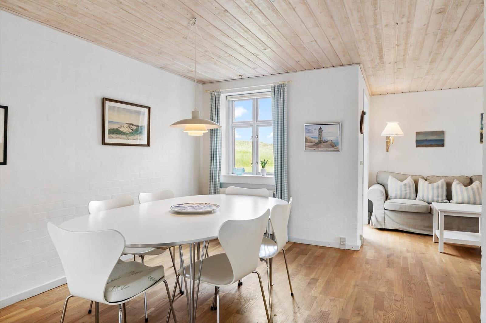 Essbereich mit runder Tisch und Stühlen. Wohnbereich mit Sofa und Couchtisch. Holzdecke und Fenster.