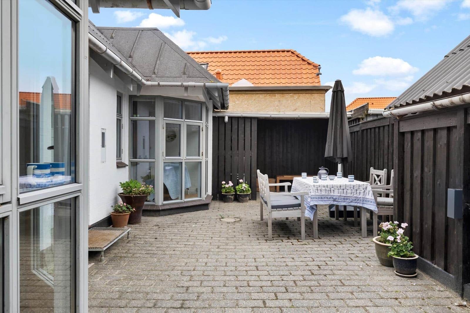 Hinterhof mit Tisch, Stühlen und Sonnenschirm. Pflanzen und gepflasterte Fläche.