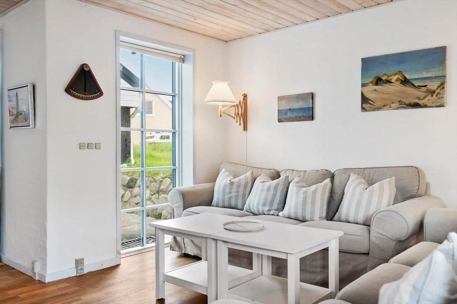 Wohnzimmer mit Sofa, Tisch und Fenster. Wandbilder und Holzdecke.