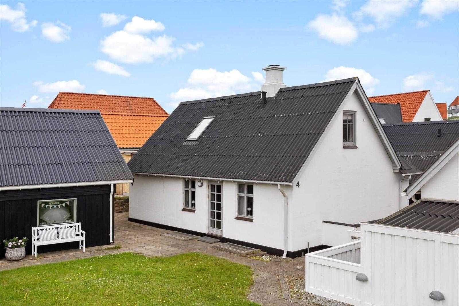 Weiße Villa mit schwarzem Dach, Garten und Terrasse. Hinterhof mit weißem Zaun.