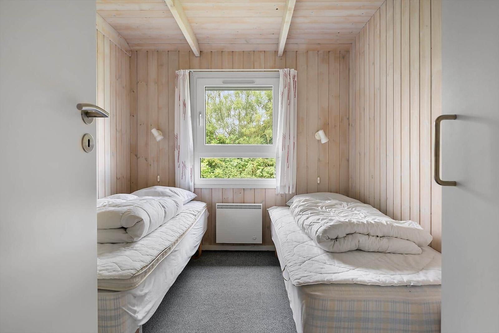 Zwei Einzelbetten in einem Raum mit Holzwänden und Fenster. Heizung und Vorhänge sind sichtbar.