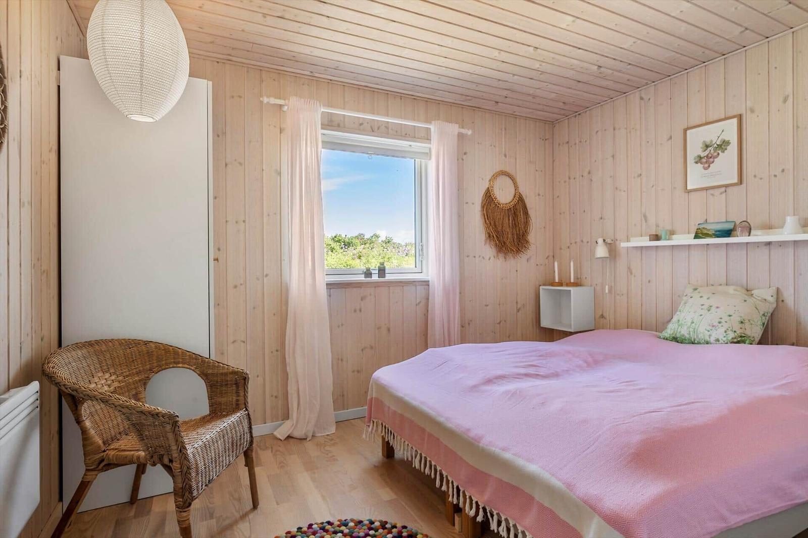 Schlafzimmer mit Bett, Stuhl und Fenster mit Blick auf Grün.