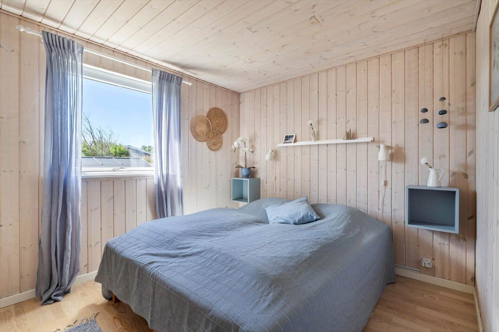 Schlafzimmer mit Holzwand, Bett und Fenster. An der Wand hängen Regale und Dekoration.