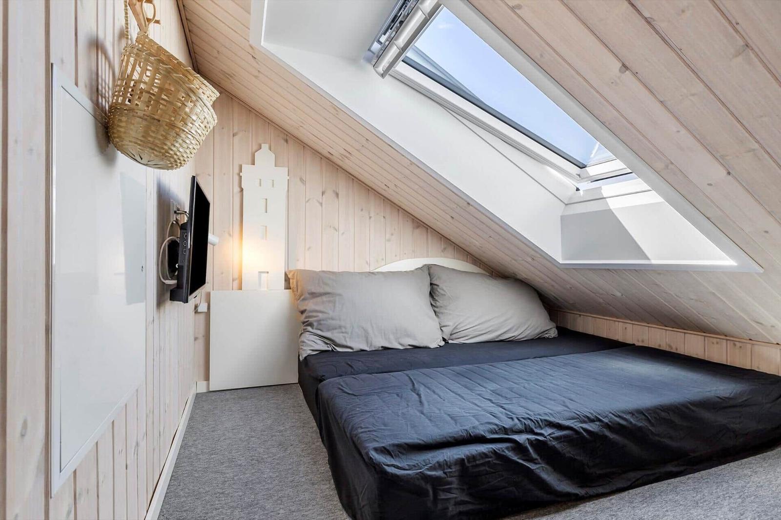 Schlafzimmer mit Dachfenster, Bett und Fernseher an der Wand.