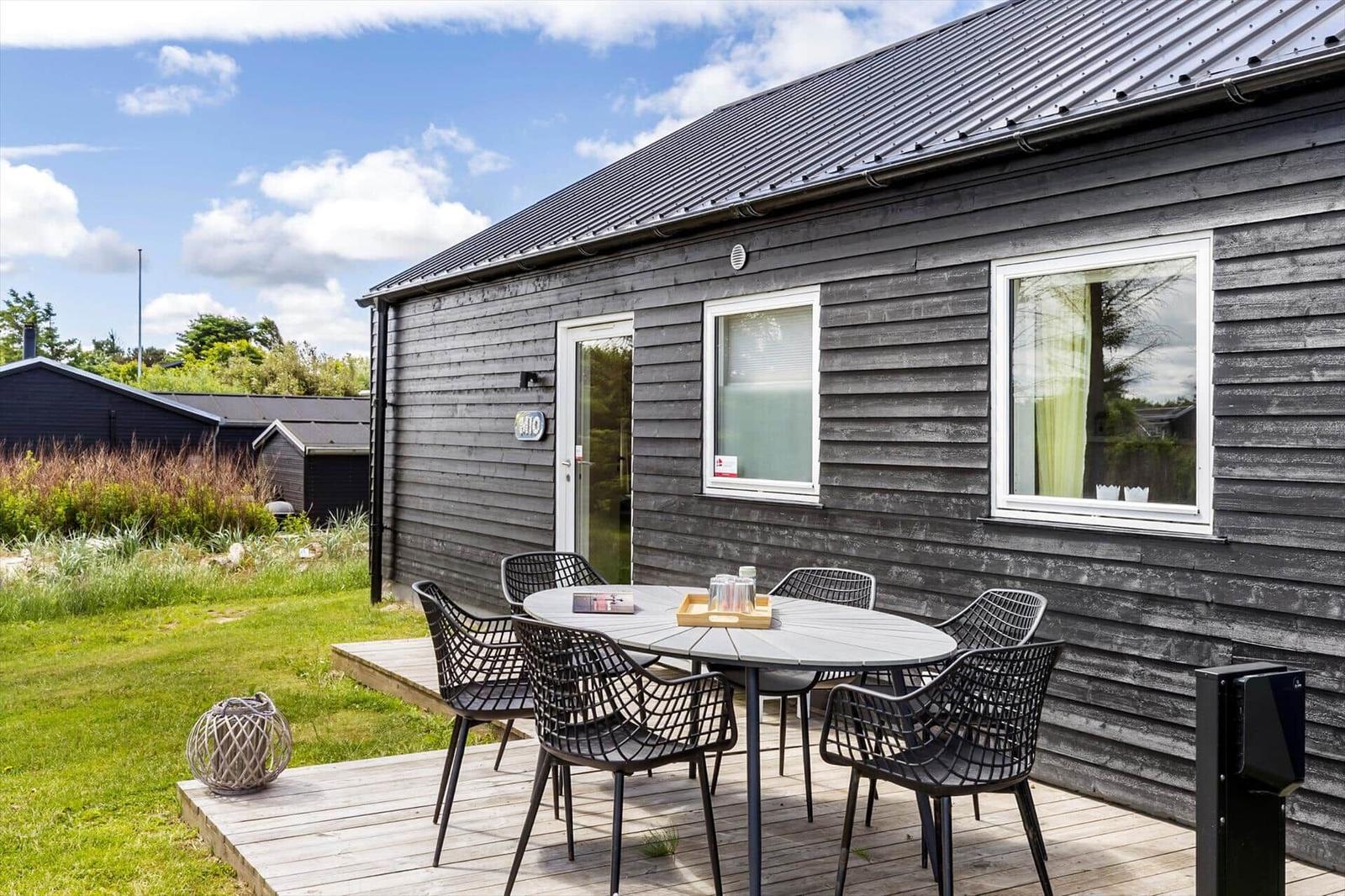 Graues Holzhaus mit Terrasse und Sitzgruppe. Garten und Himmel sind sichtbar.