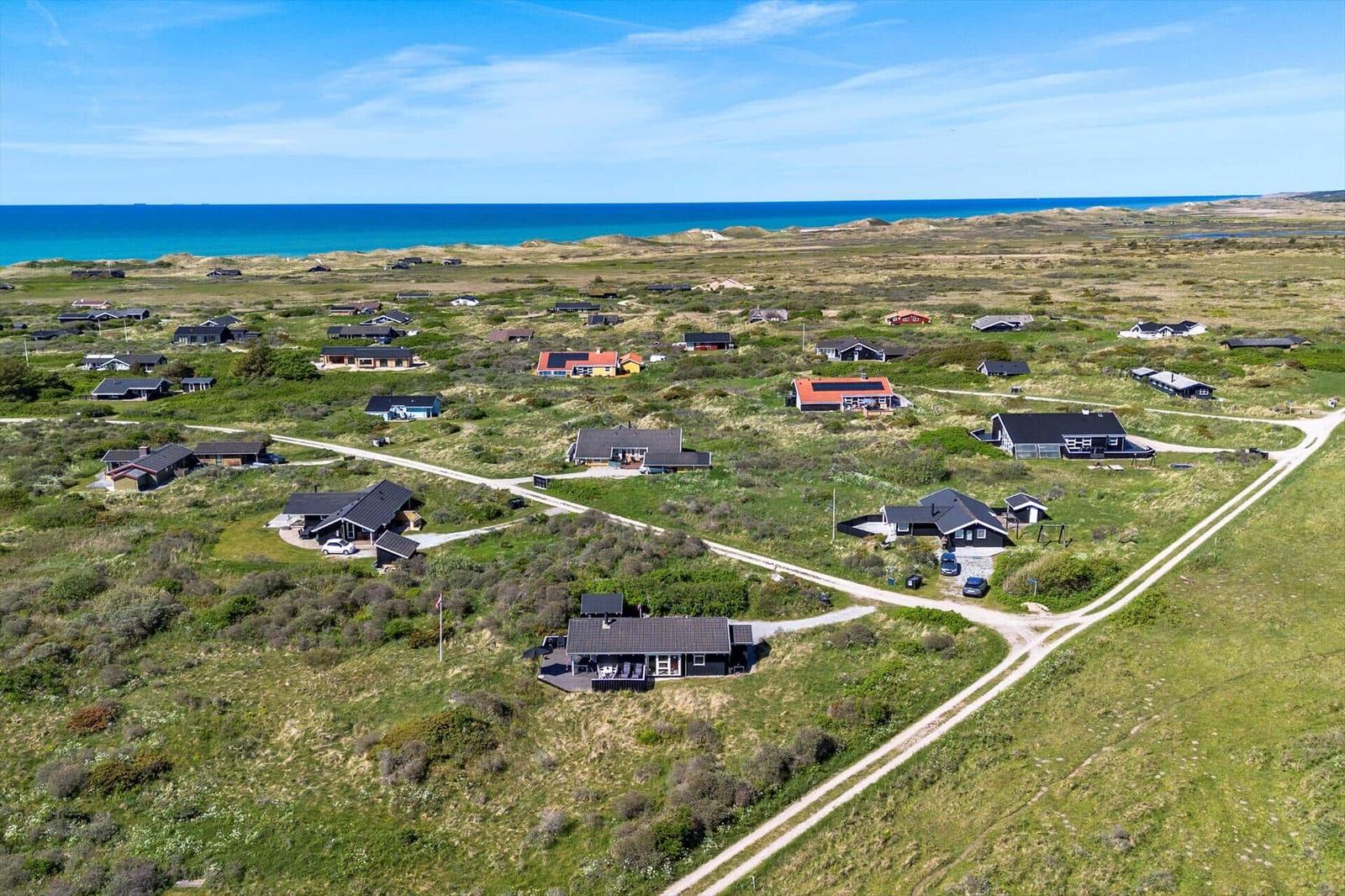 Aeriale Aufnahme von Ferienhäusern in einer grünen Landschaft mit Blick auf das Meer.