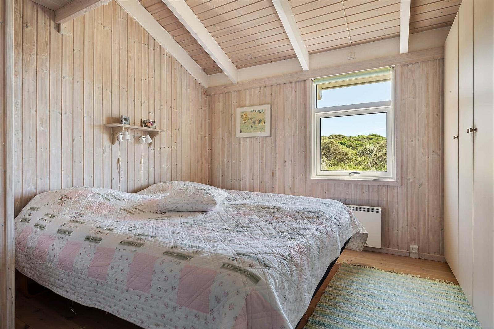 Schlafzimmer mit Holzwand und Fensterblick auf Grünflächen
