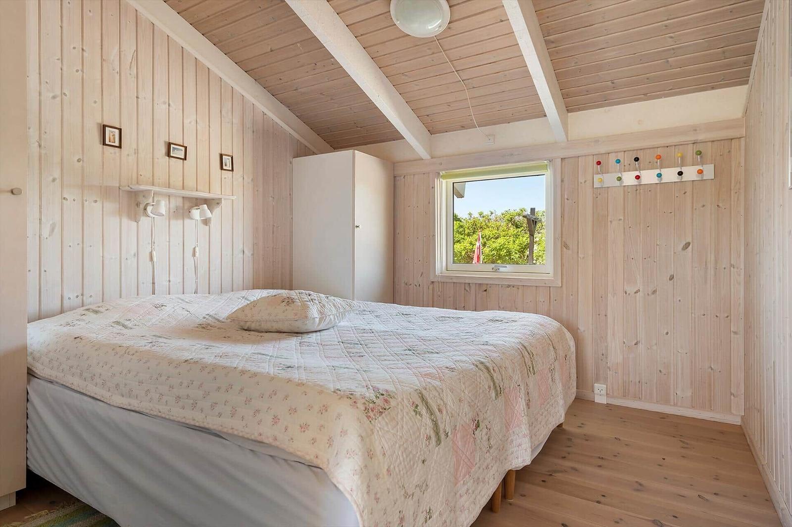Schlafzimmer mit Bett, Kleiderhaken und Fenster zum Garten.