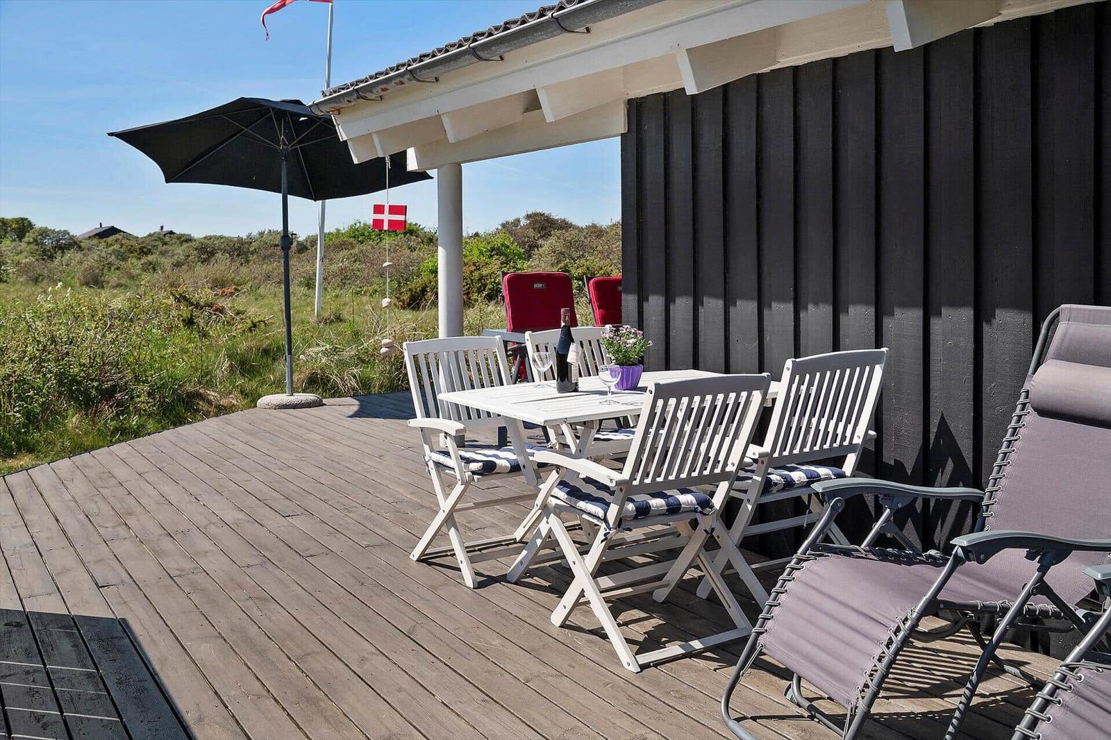 Terrasse mit Tisch, Stühlen und Sonnenschirm. Blick auf Grünland und Flagge.