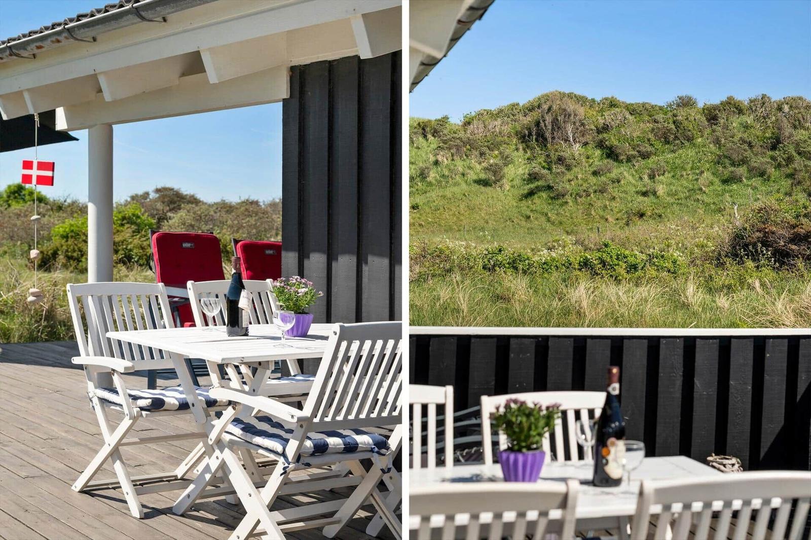 Terrasse mit Tisch, Stühlen und Blick auf grüne Hügel. Daneben hängt eine dänische Flagge.