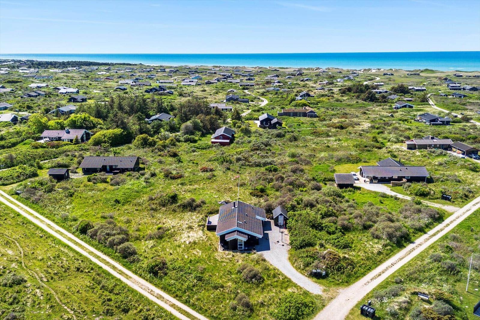 Übersicht über Ferienhäuser auf einer grünen Dünenlandschaft mit Blick auf das Meer.