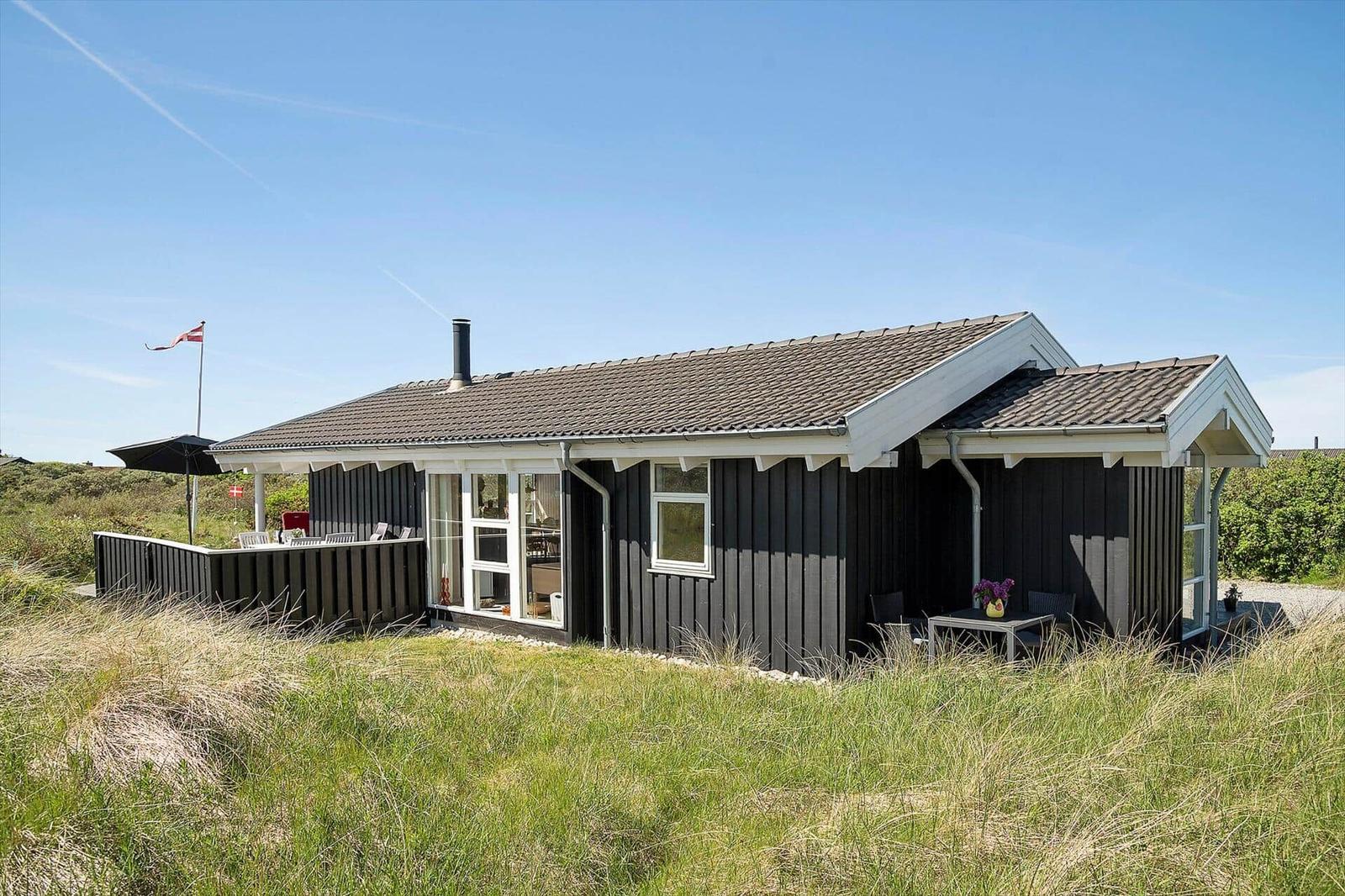 Ein schwarz getäfeltes Haus mit weißem Rahmen und Dach, umgeben von Gras und einem kleinen Balkon.